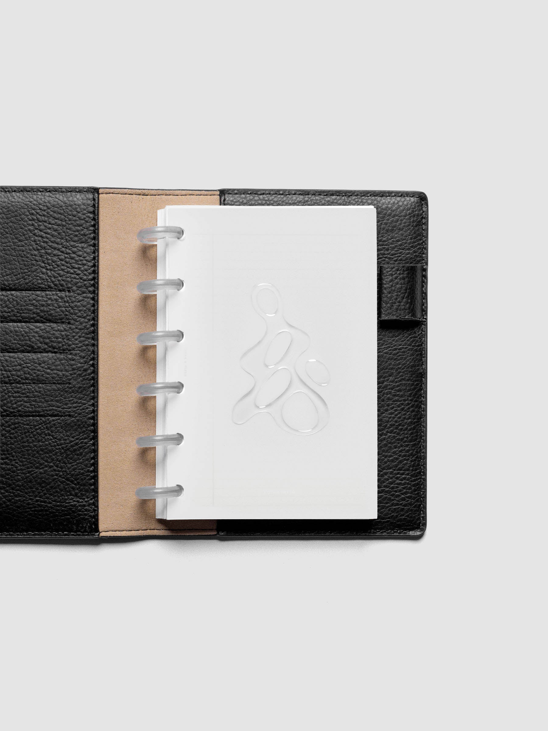 Light grey, semi-transparent, and glossy plastic planner dashboard with organic raised shape design in size CP Petite shown discbound in a black leather folio.