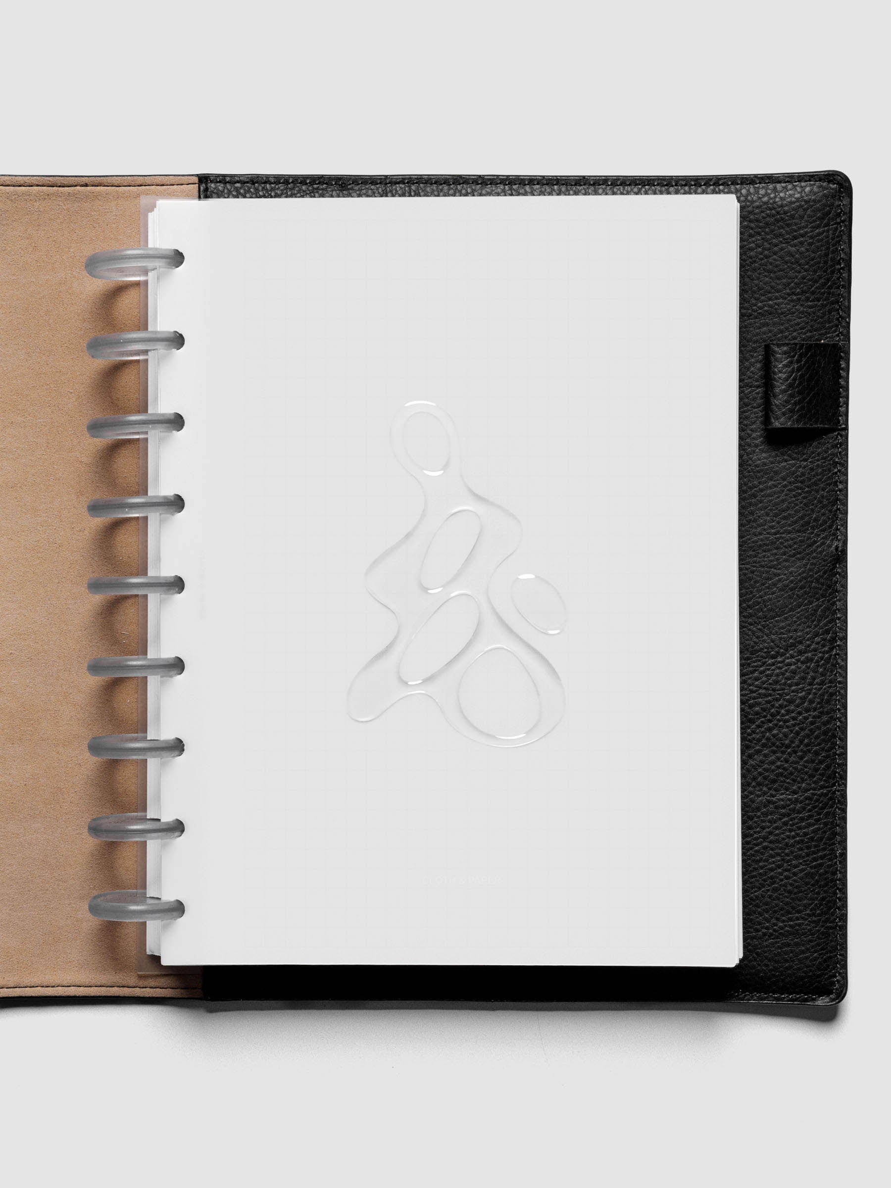 Light grey, semi-transparent, and glossy plastic planner dashboard with organic raised shape design in size HP Classic shown discbound in a black leather folio.