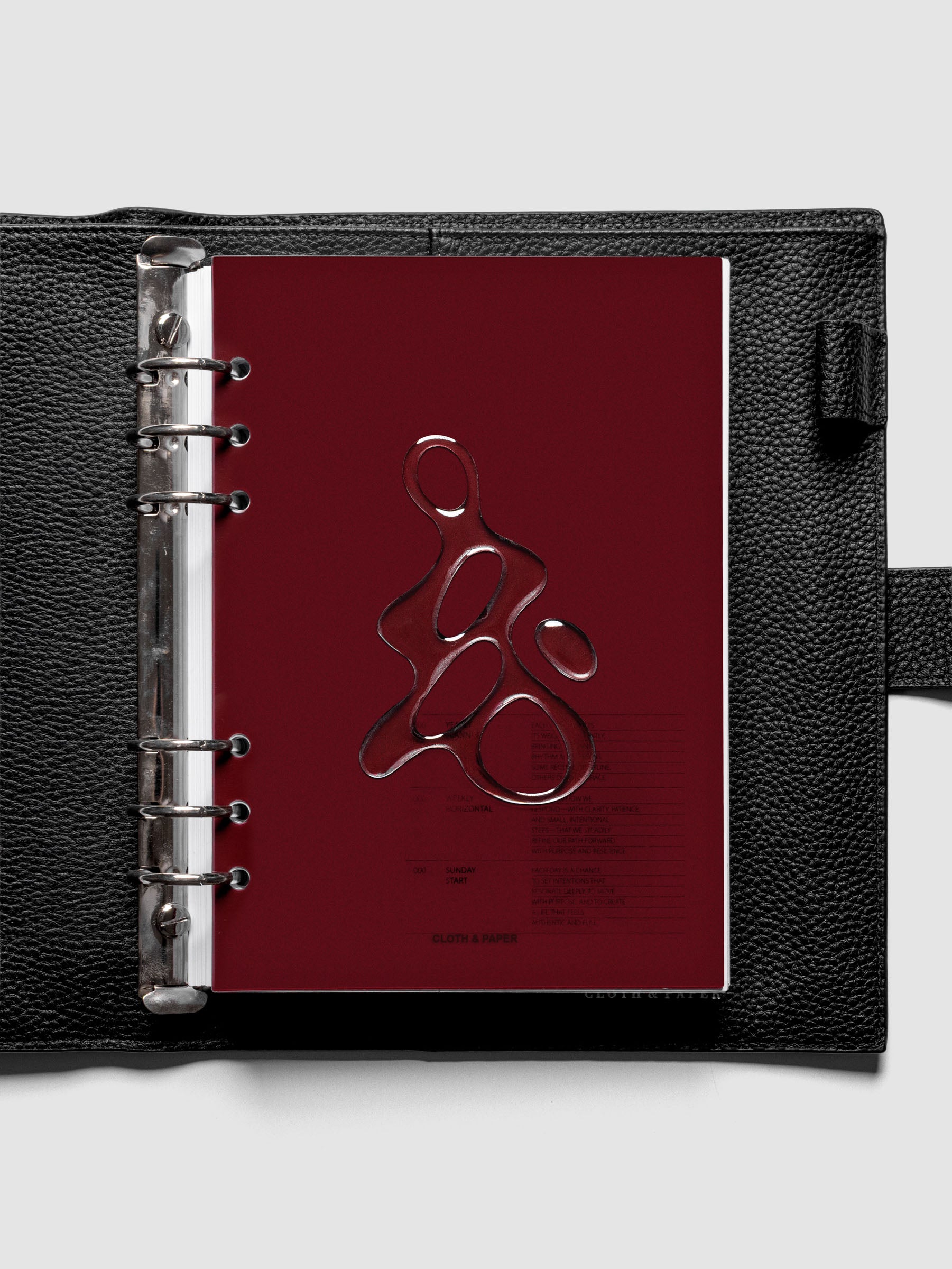 Dark red, semi-transparent, and glossy plastic planner dashboard with organic raised shape design in size A5 shown ringbound in a black leather agenda.