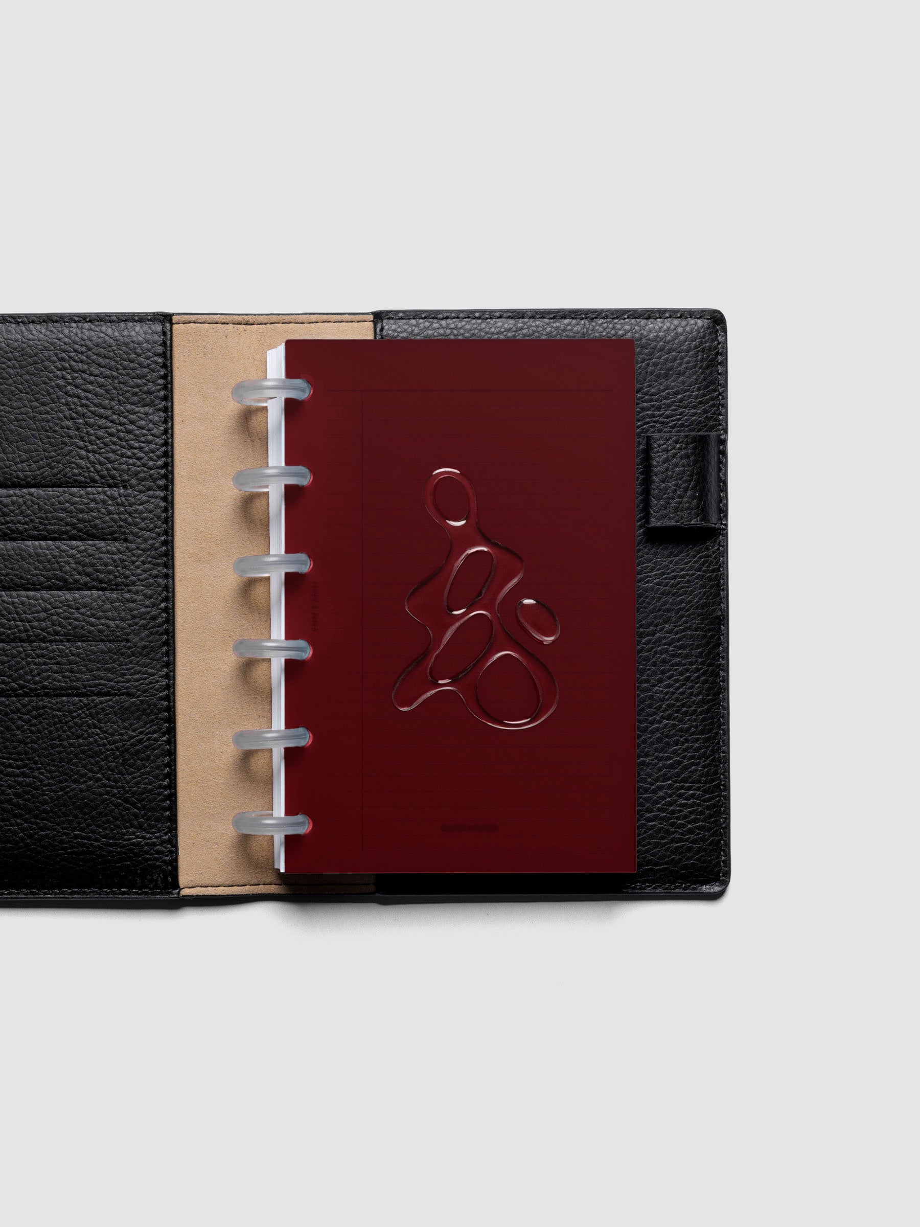 Dark red, semi-transparent, and glossy plastic planner dashboard with organic raised shape design in size CP Petite shown discbound in a black leather folio.