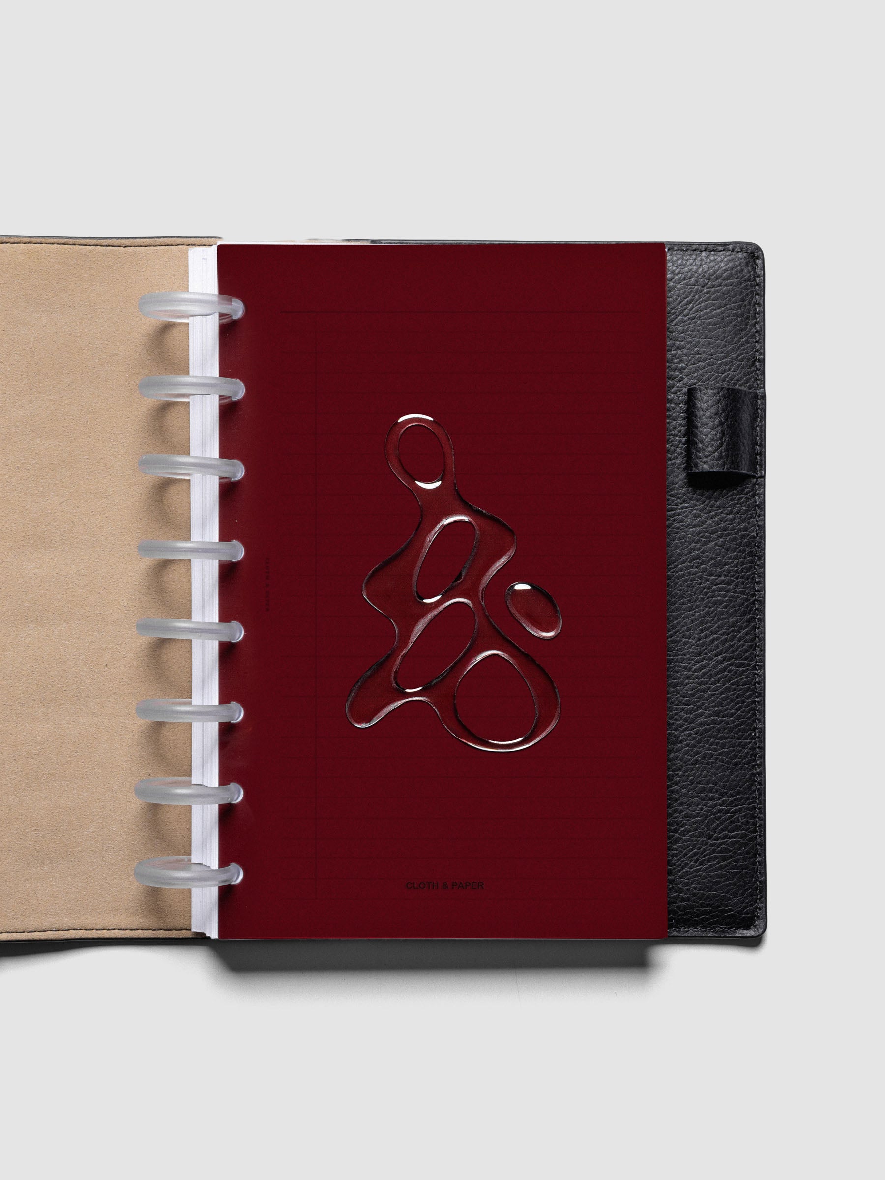 Dark red, semi-transparent, and glossy plastic planner dashboard with organic raised shape design in size Half Letter shown discbound in a black leather folio.