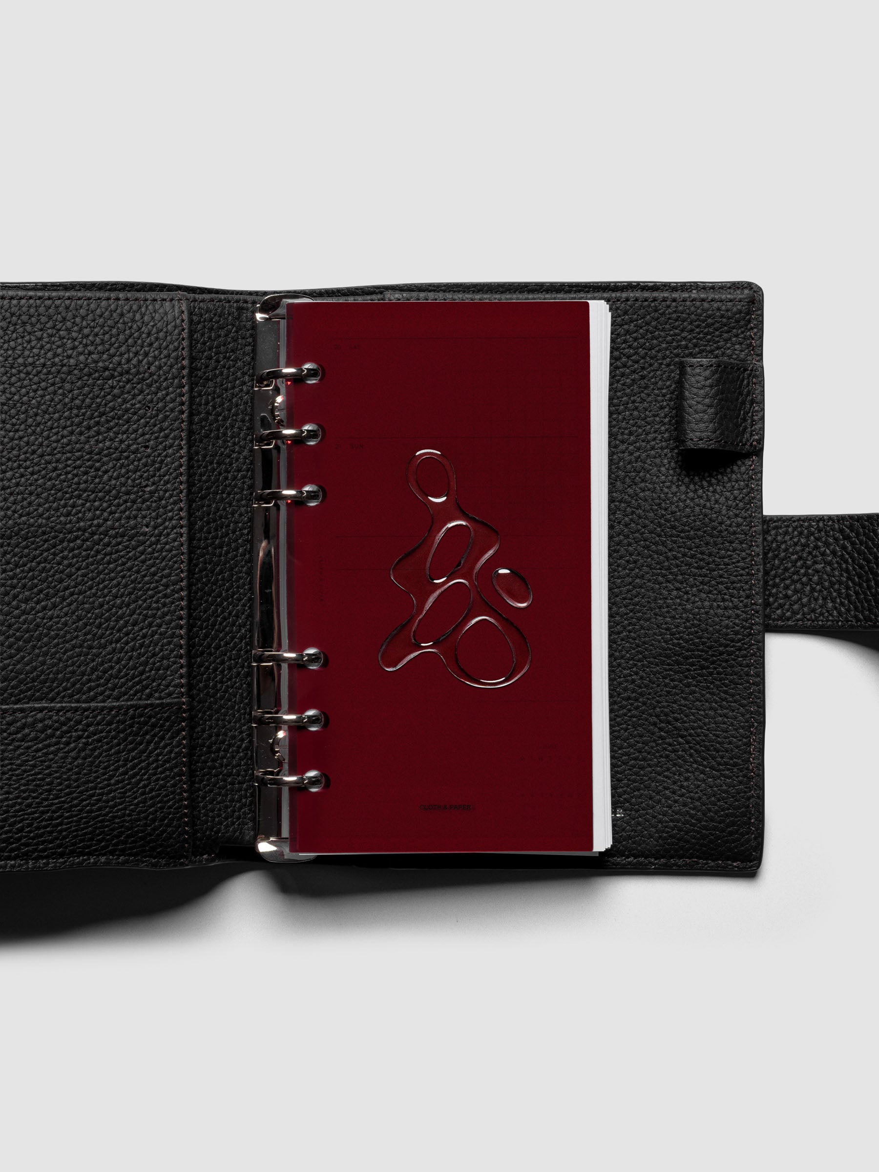 Dark red, semi-transparent, and glossy plastic planner dashboard with organic raised shape design in size Personal shown ringbound in a black leather agenda.