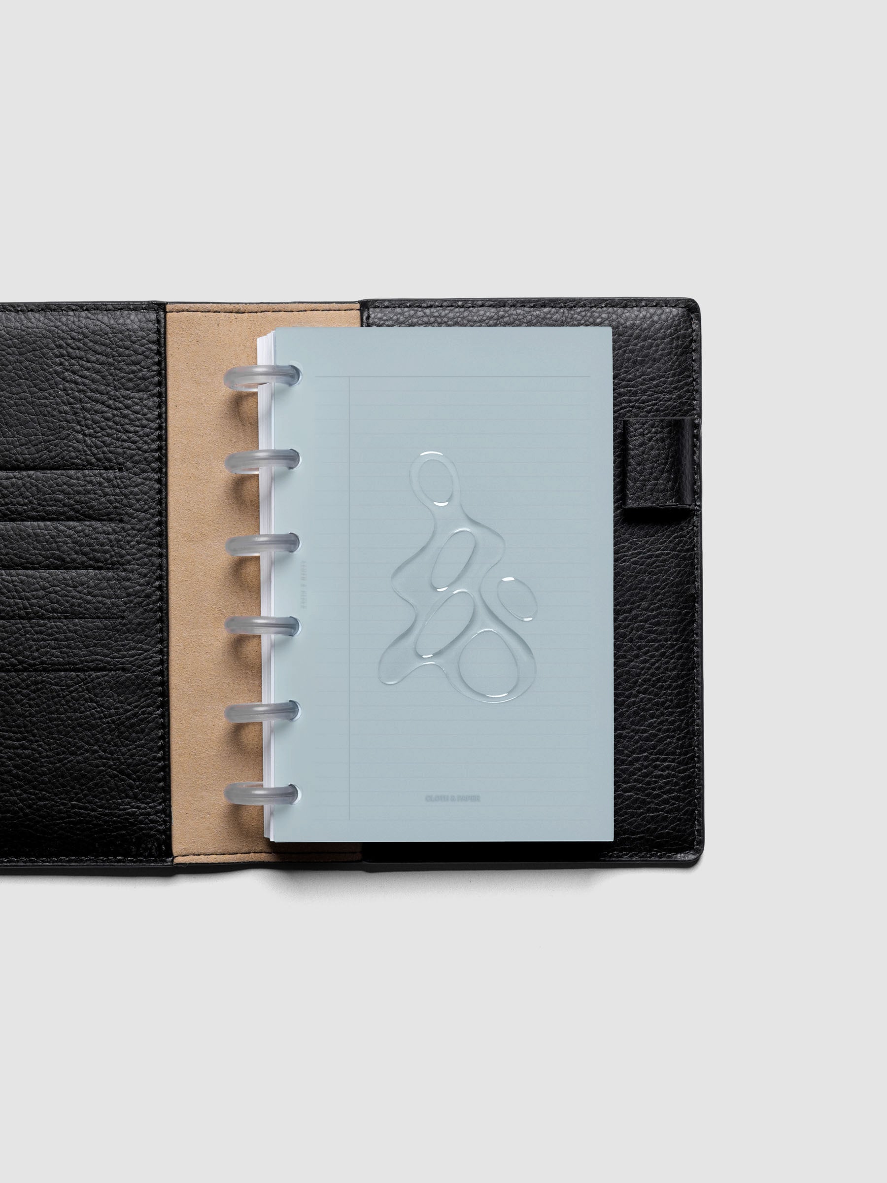 Light blue, semi-transparent, and glossy plastic planner dashboard with organic raised shape design in size CP Petite shown discbound in a black leather folio.