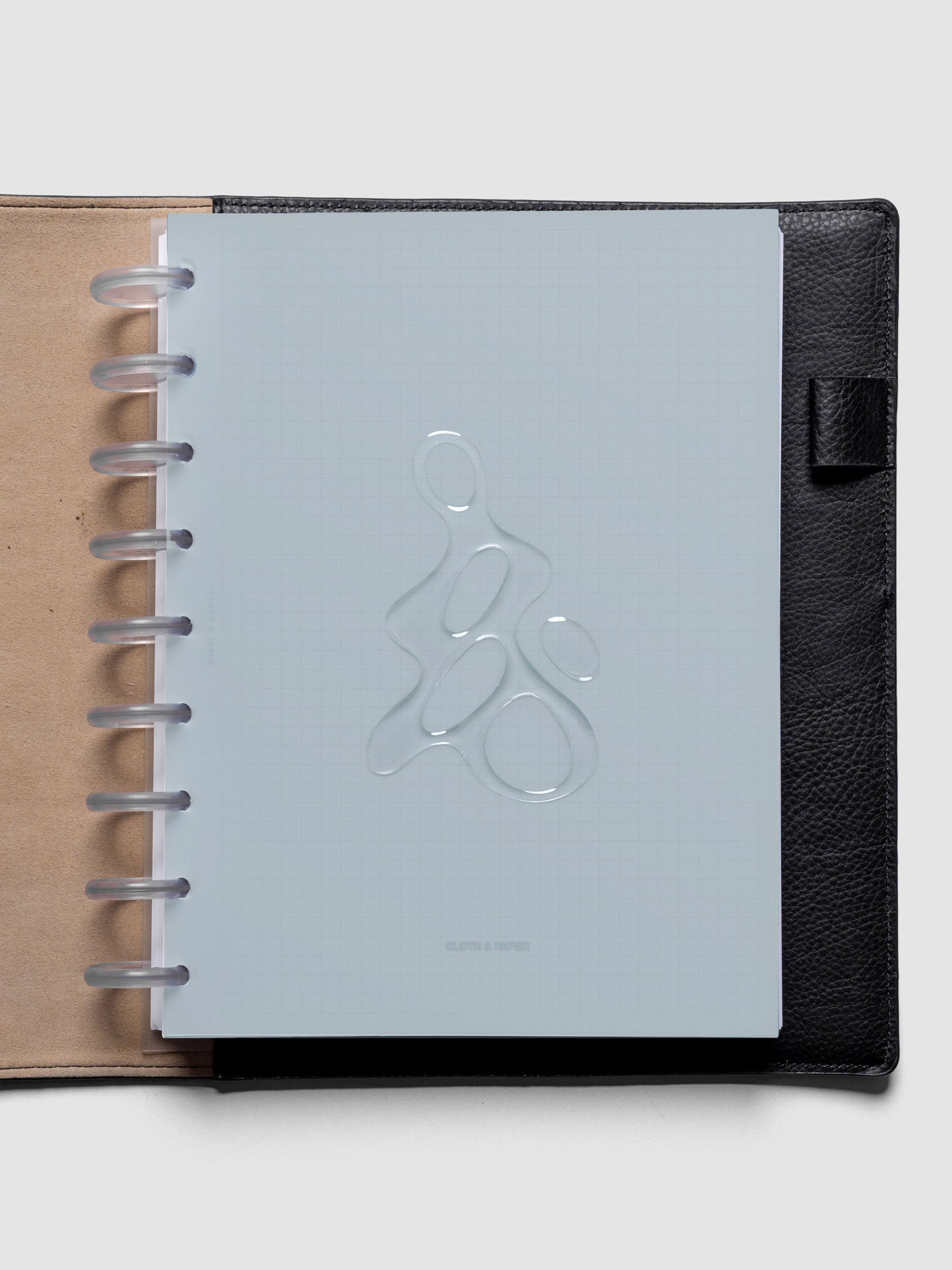 Light blue, semi-transparent, and glossy plastic planner dashboard with organic raised shape design in size HP Classic shown discbound in a black leather folio.