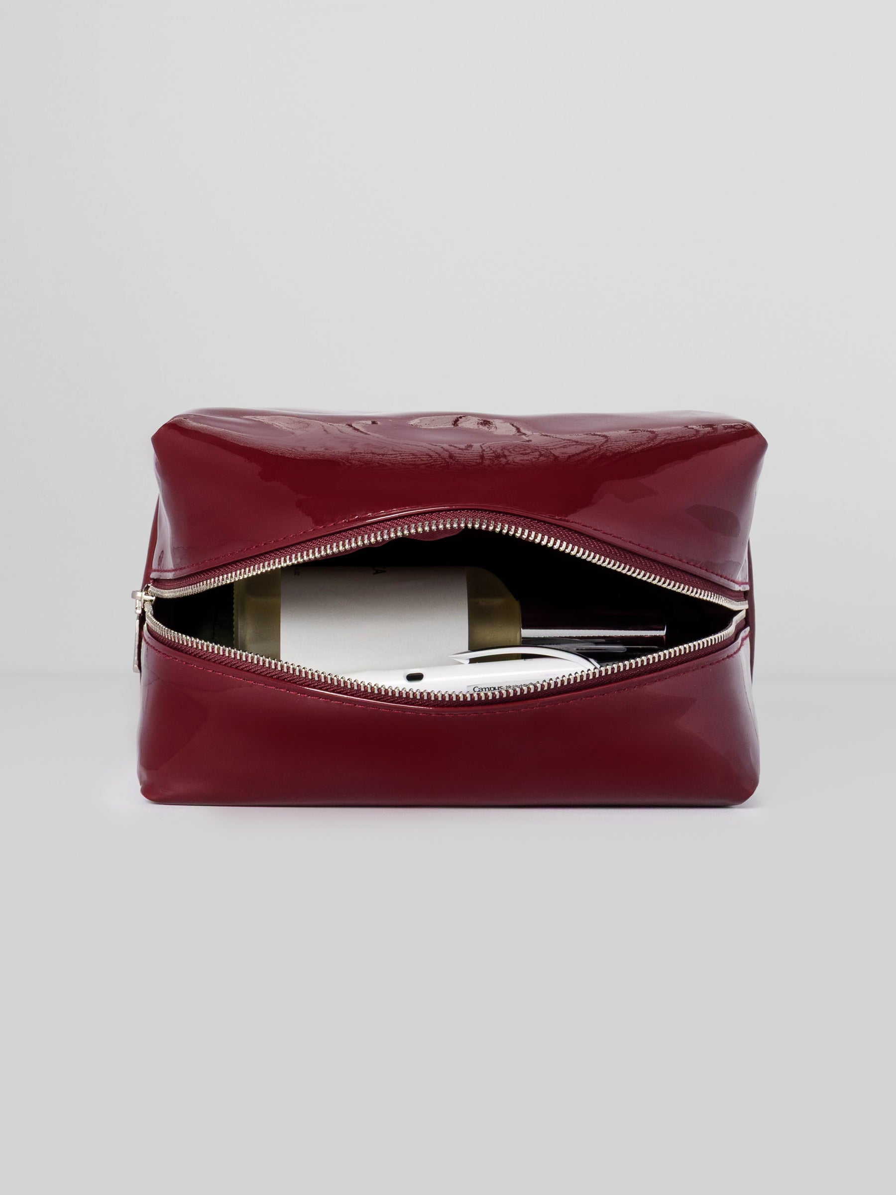 Deep red Lacquered Pouch shown laid down, with the zipper open, and contents inside.