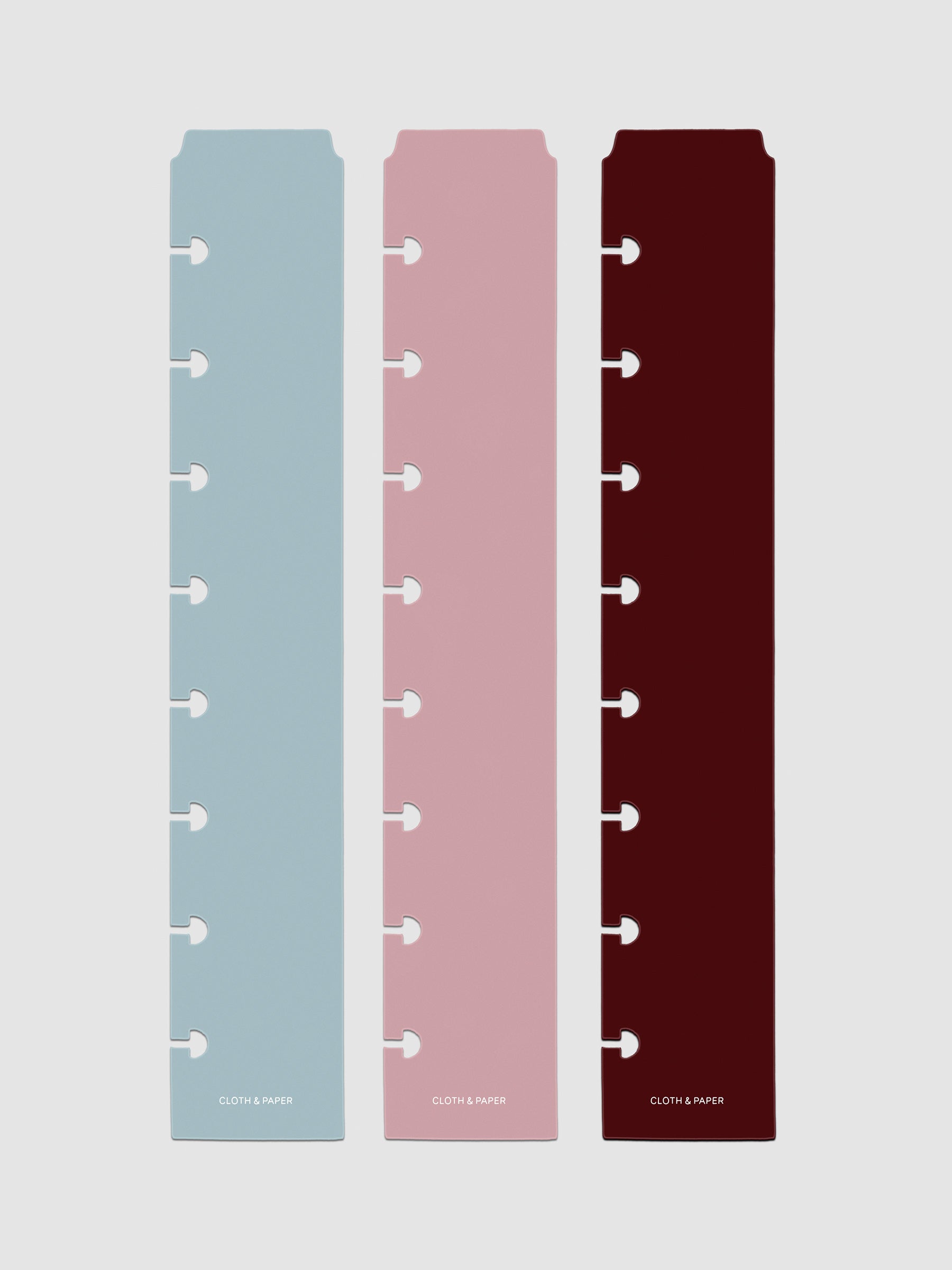 Set of three narrow page markers pre-punched for discbound planners in light blue, pink, and burgundy on a neutral background.