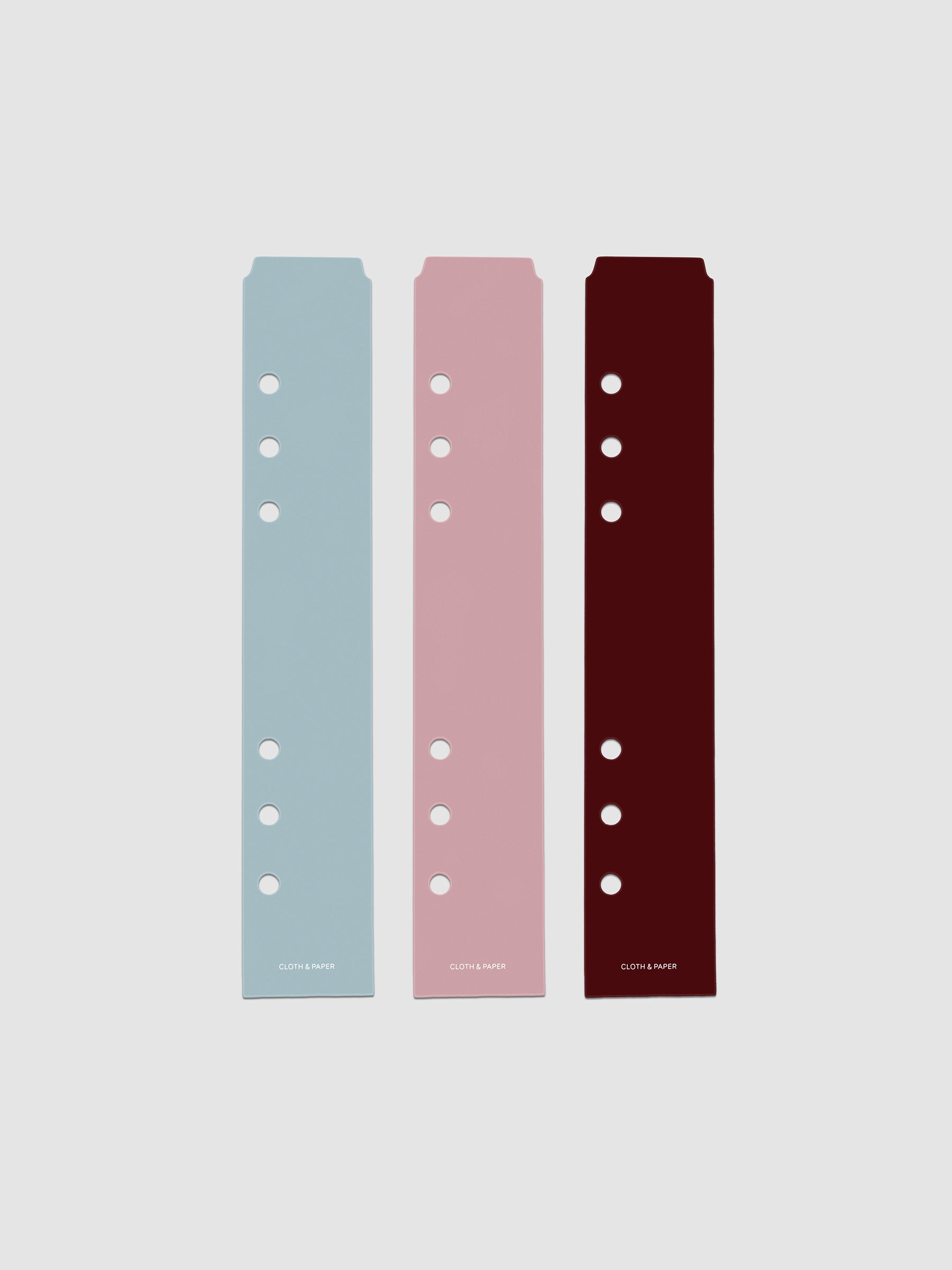 Set of three narrow page markers pre-punched for A5 planners in light blue, pink, and burgundy on a neutral background.