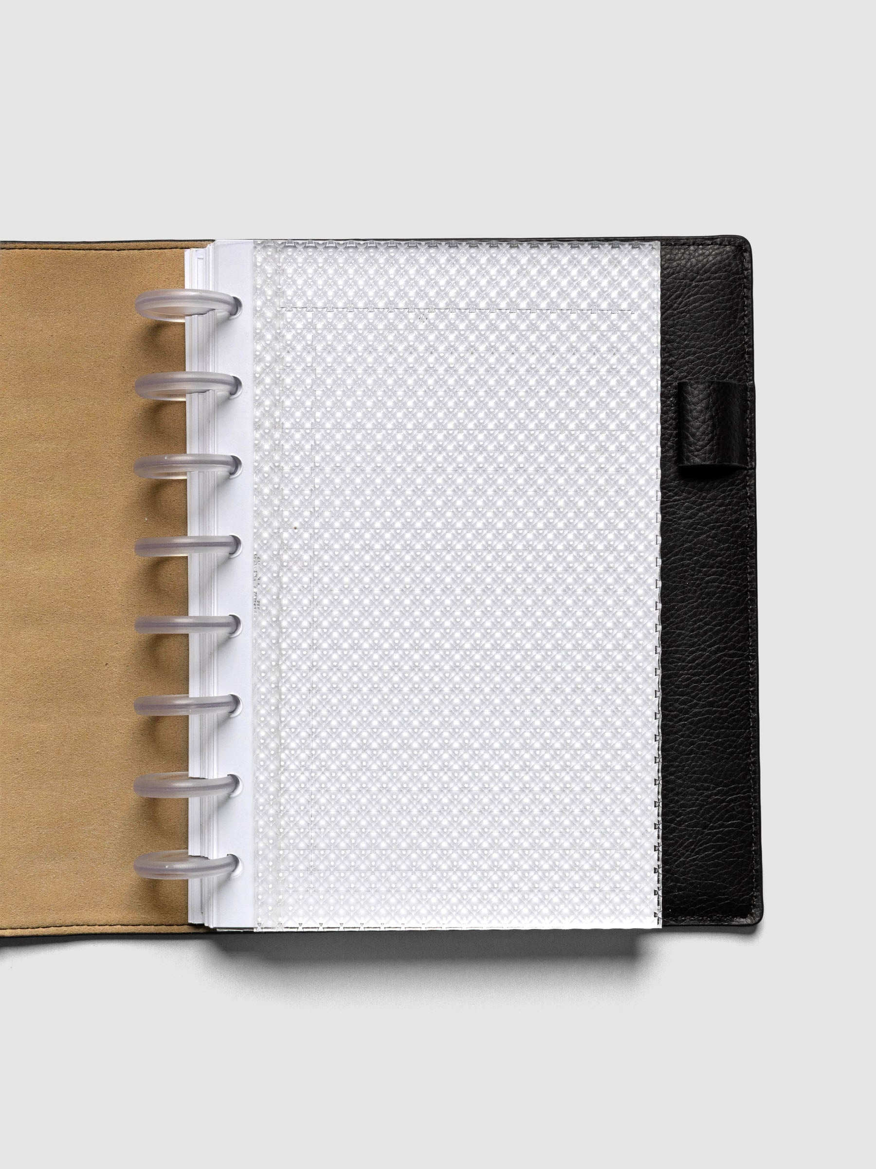 Clear, textured Studded Planner Dashboard in the size Half Letter, shown discbound in a leather folio on a neutral background.