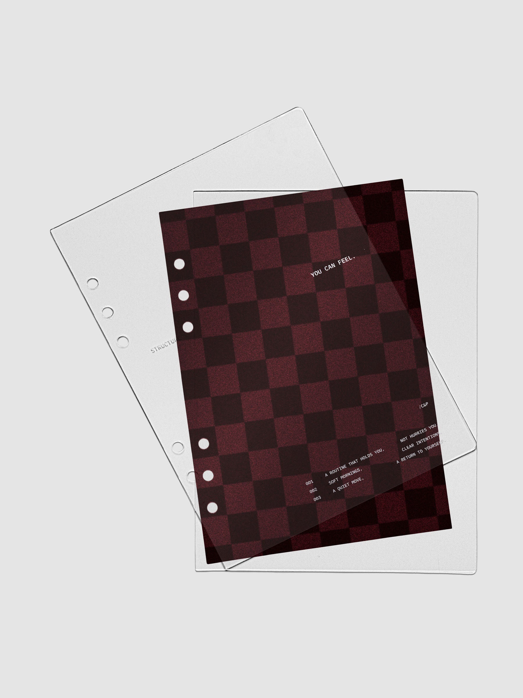A5 sized velvet checkered dashboard in the color Bordeaux in between two crystal clear plastic planner covers with text printed on the cover on the theme of structure and routines.