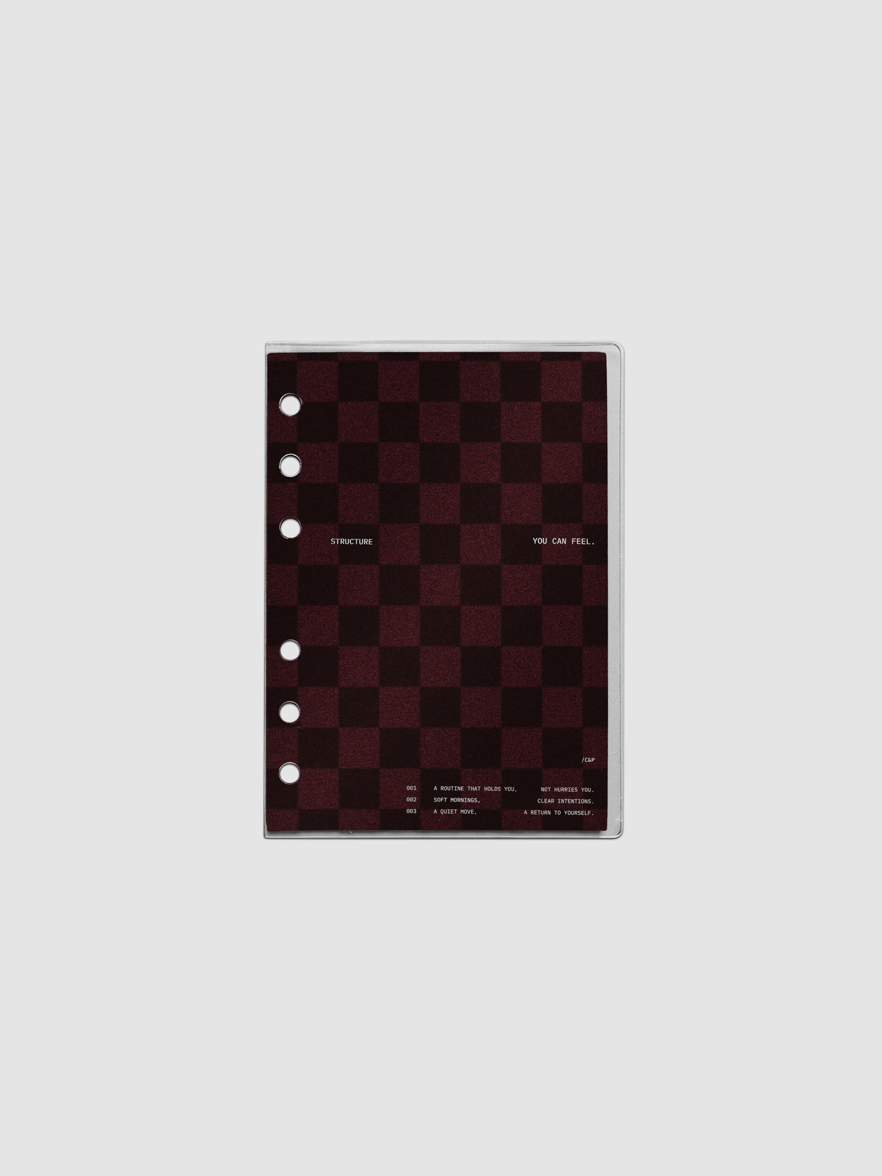 A6 sized velvet checkered dashboard in the color Bordeaux in between two crystal clear plastic planner covers with text printed on the cover on the theme of structure and routines.