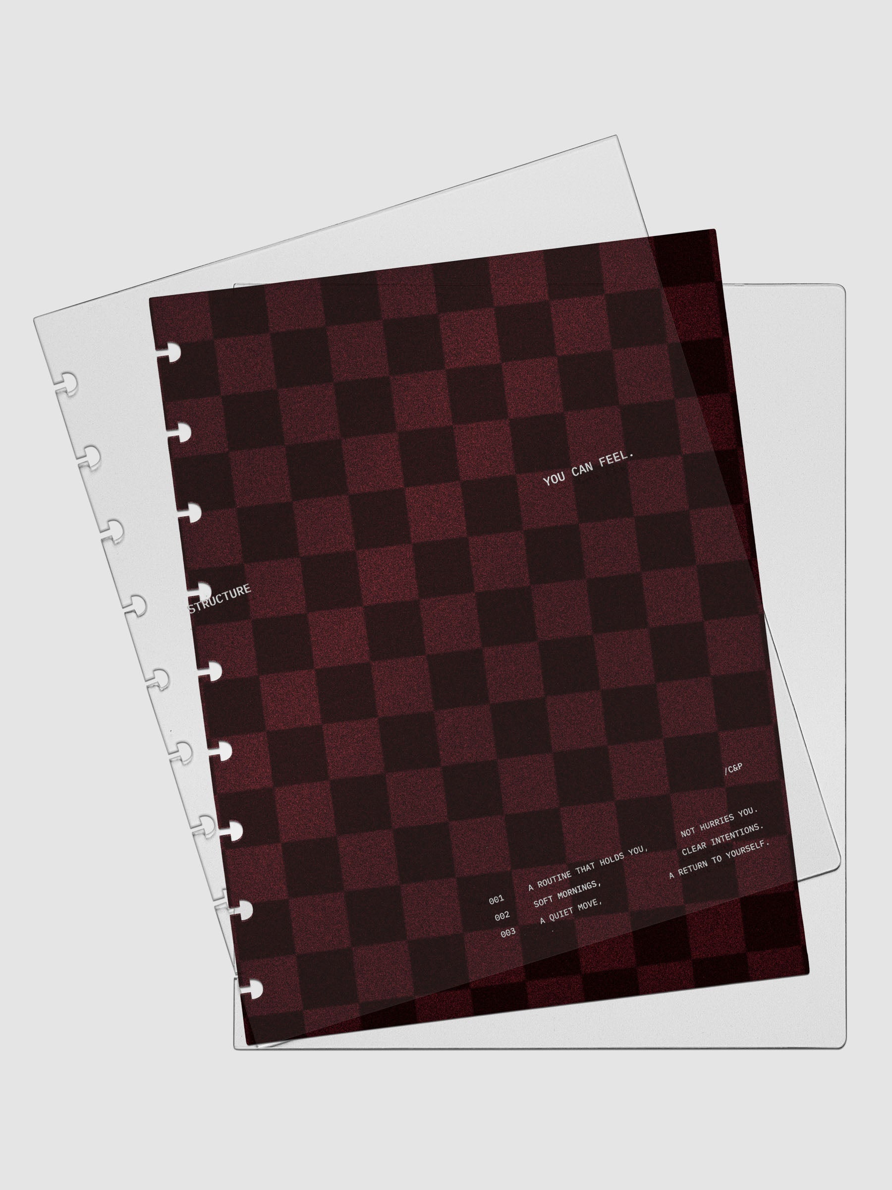 HP Classic sized velvet checkered dashboard in the color Bordeaux in between two crystal clear plastic planner covers with text printed on the cover on the theme of structure and routines.