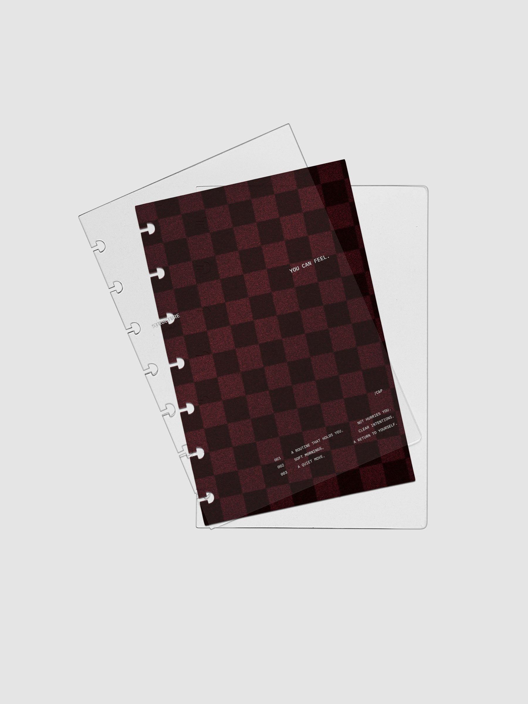 HP Mini sized velvet checkered dashboard in the color Bordeaux in between two crystal clear plastic planner covers with text printed on the cover on the theme of structure and routines.