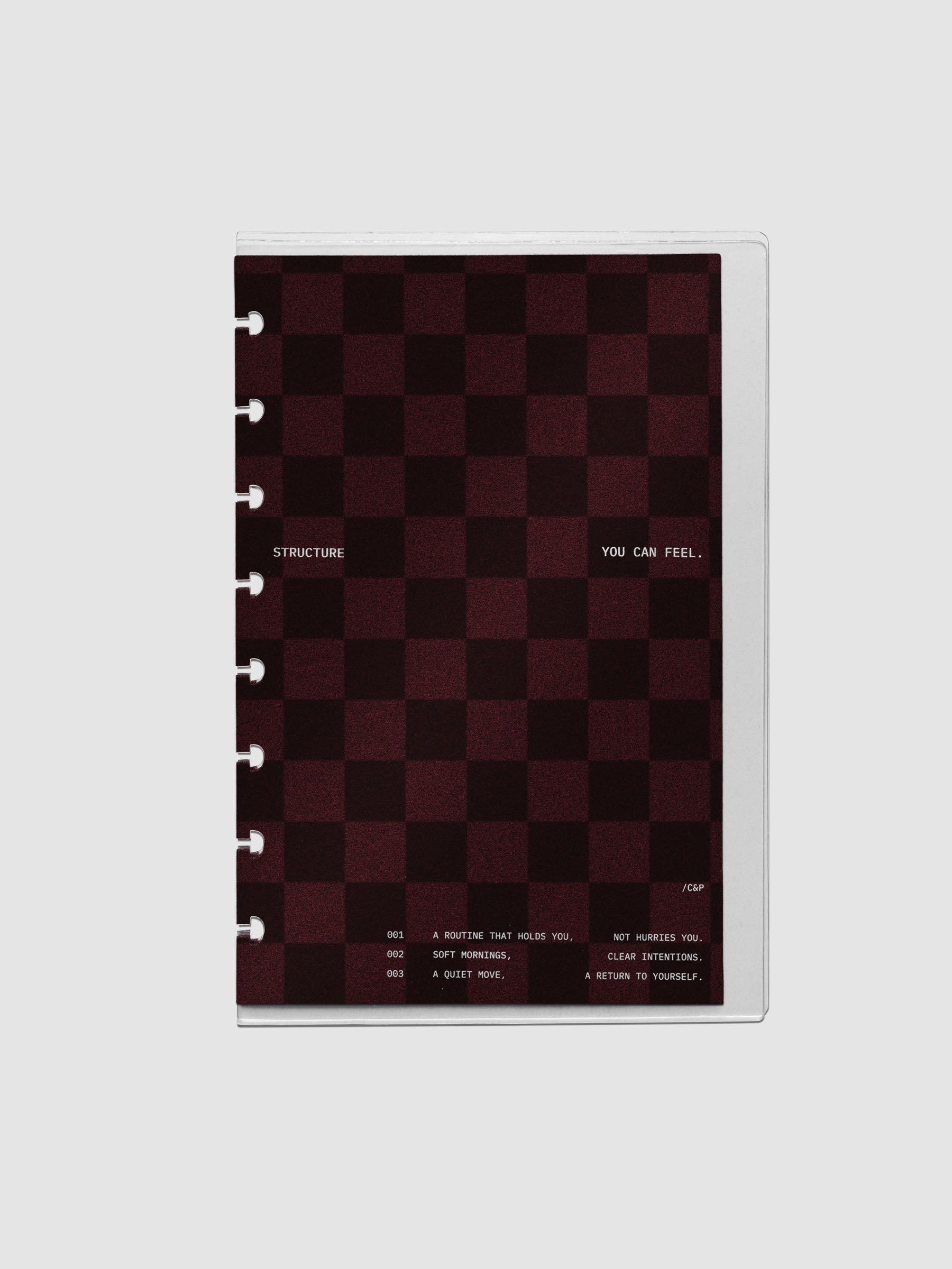 Half Letter sized velvet checkered dashboard in the color Bordeaux in between two crystal clear plastic planner covers with text printed on the cover on the theme of structure and routines.