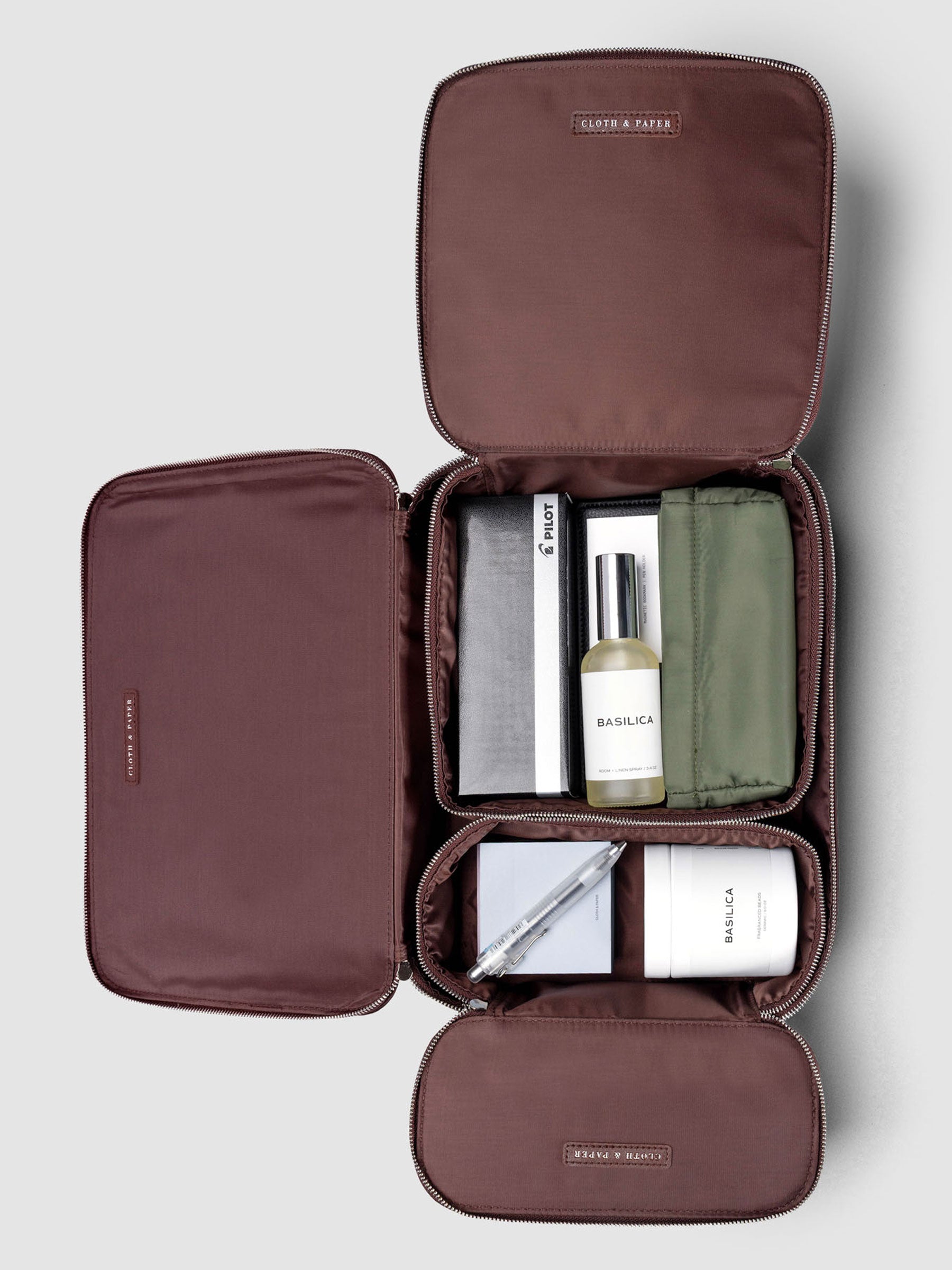 Set of three nesting packing cubes in small, medium, and large in the color walnut on a neutral background with various Cloth & Paper products nestled inside.