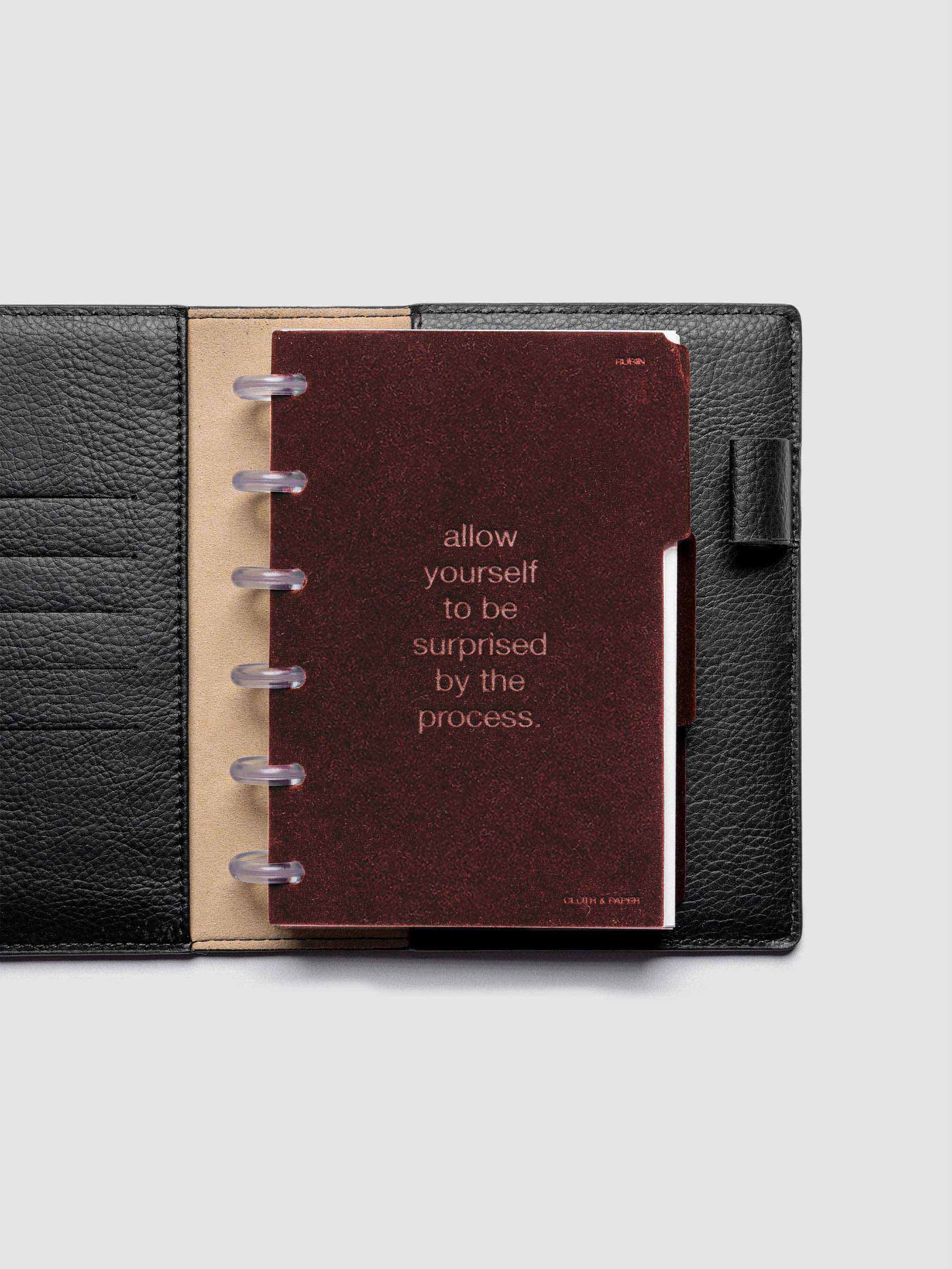 First velvet side tab planners dividers in the color Bordeaux with text deboss design reading "allow yourself to be surprised by the process" in size CP Petite shown discbound in a black leather folio.
