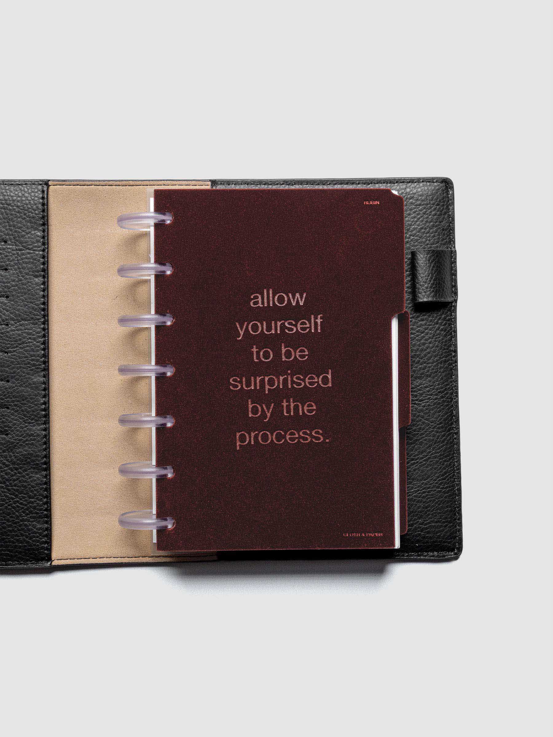 First velvet side tab planners dividers in the color Bordeaux with text deboss design reading "allow yourself to be surprised by the process" in size HP Mini shown discbound in a black leather folio.