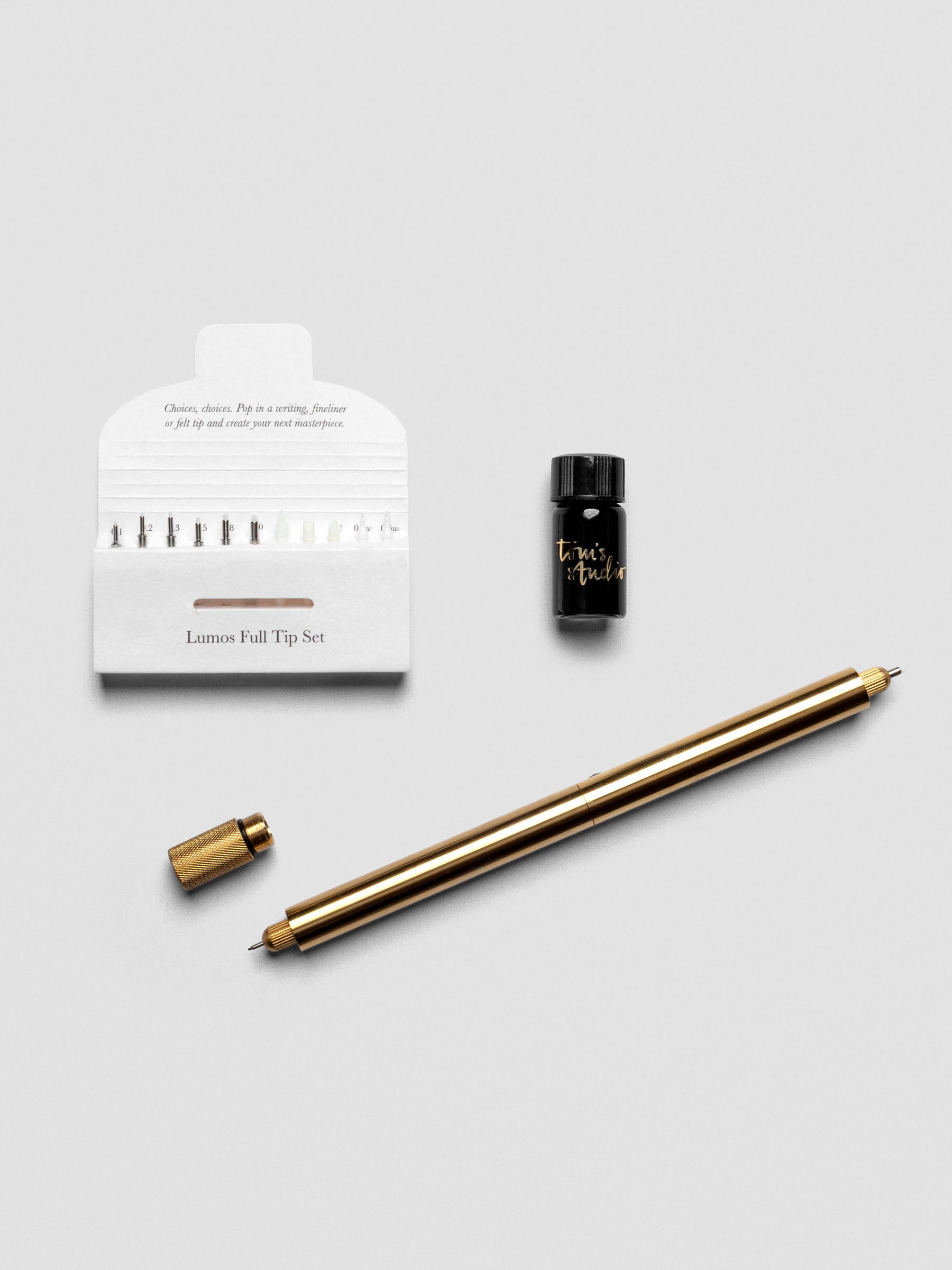 Brass Lumos Pro Duo Tip Pen resting diagonally on an open notebook, uncapped, shown with tips set and ink.