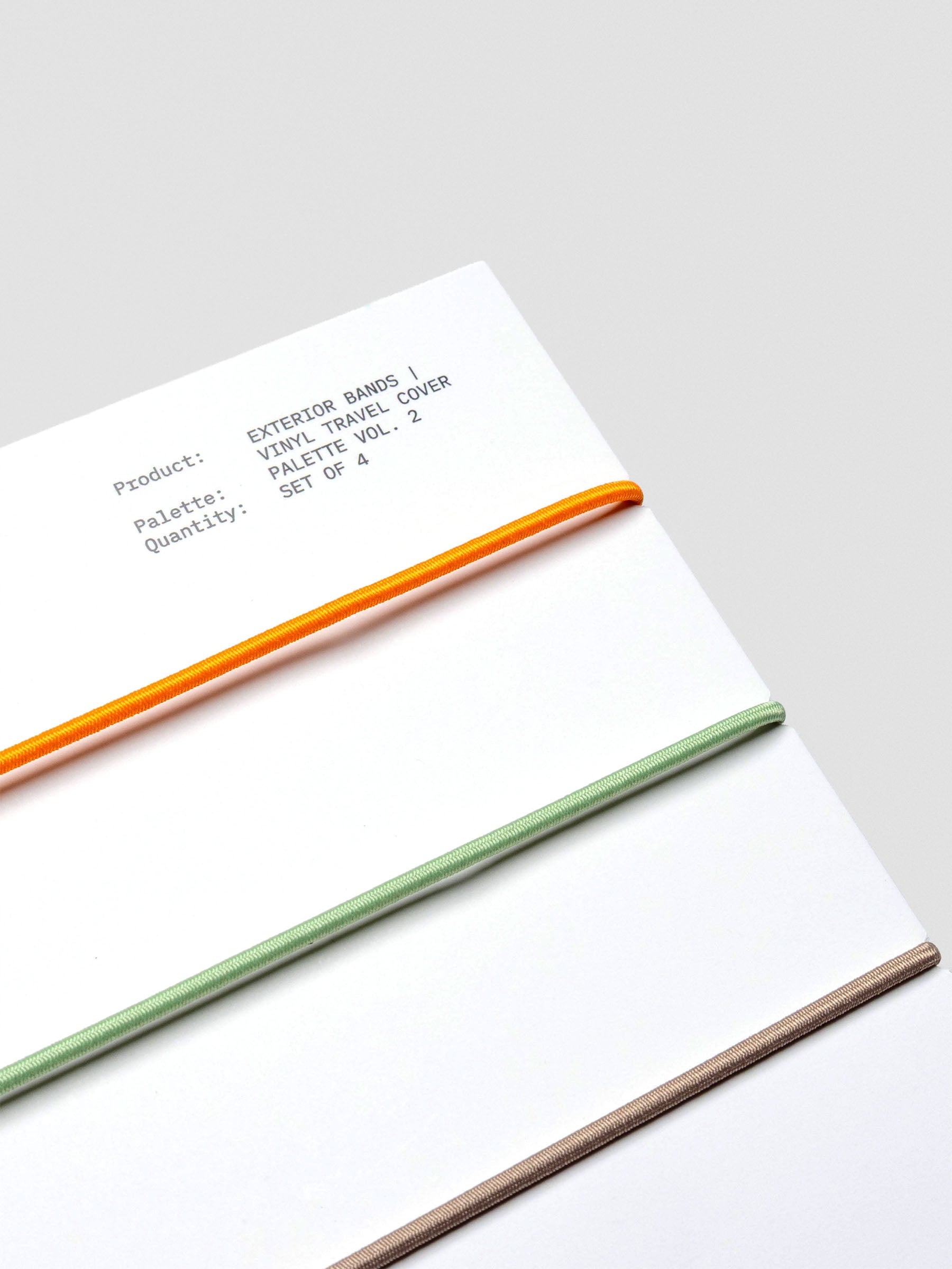 Packaging close-up showing orange, sage, dark brown, and taupe elastic bands.