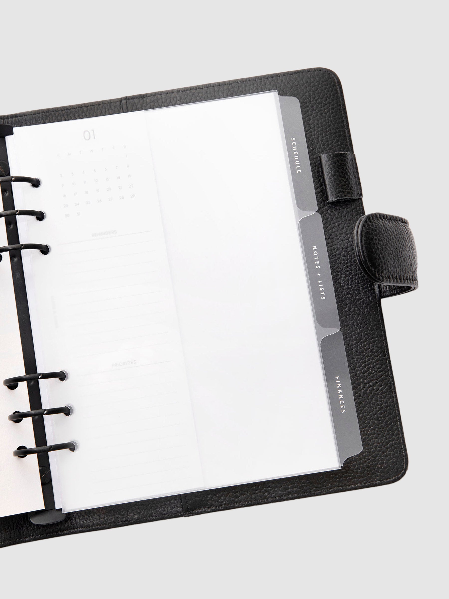 The Essentials Side Tab Planner Dividers, Glass Plastic, White Foil, Cloth and Paper. Dividers inside a planner turned slightly to the left against a neutral background.