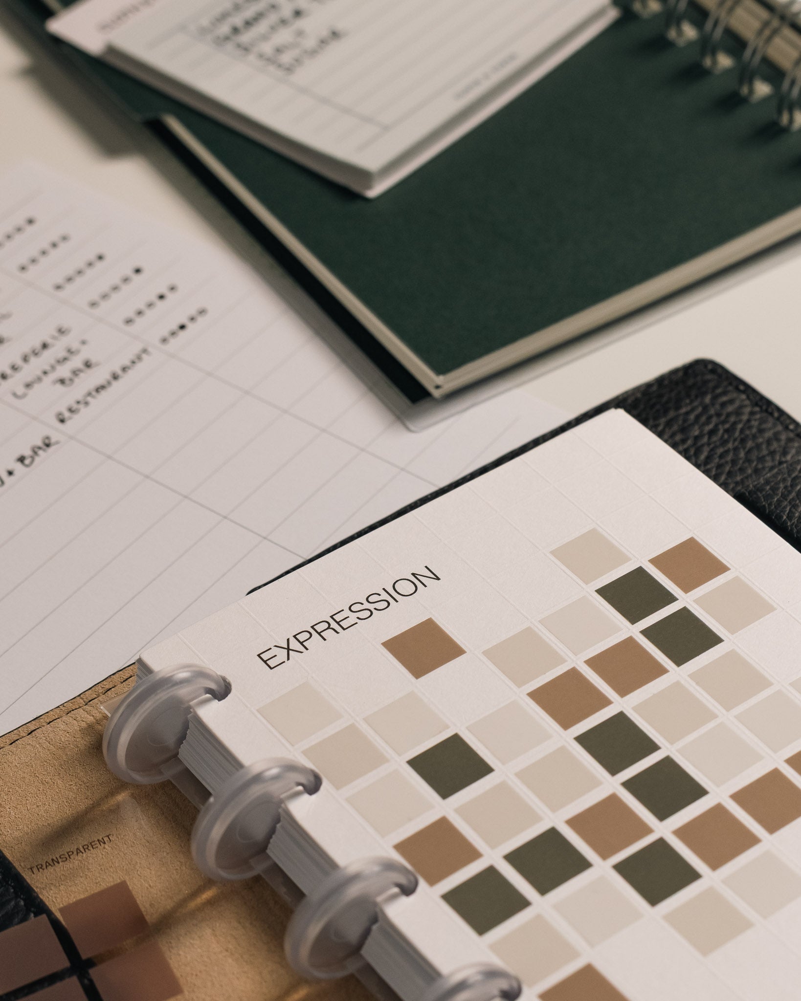 A styled desk scene with the Tile Planner Dashboard in use, embellished with Square Stickers, next to a green notebook and other stationery.