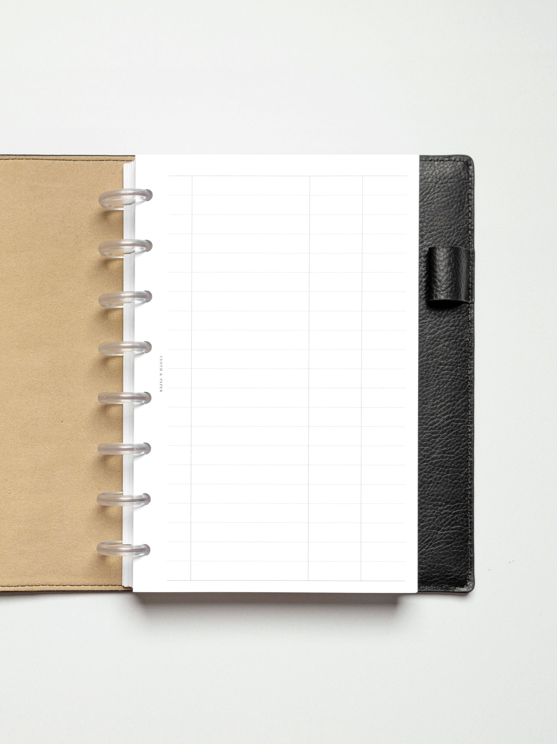 Half Letter-sized Tracker Planner Insert in a black leather discbound planner, showing an empty, gridded layout with lined sections.