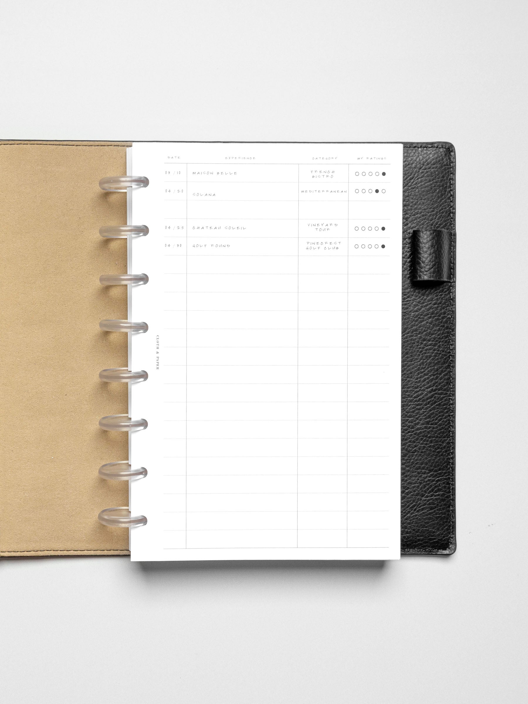 Overhead view of the Half Letter-sized Tracker Planner Insert filled in, placed in a black leather discbound planner.