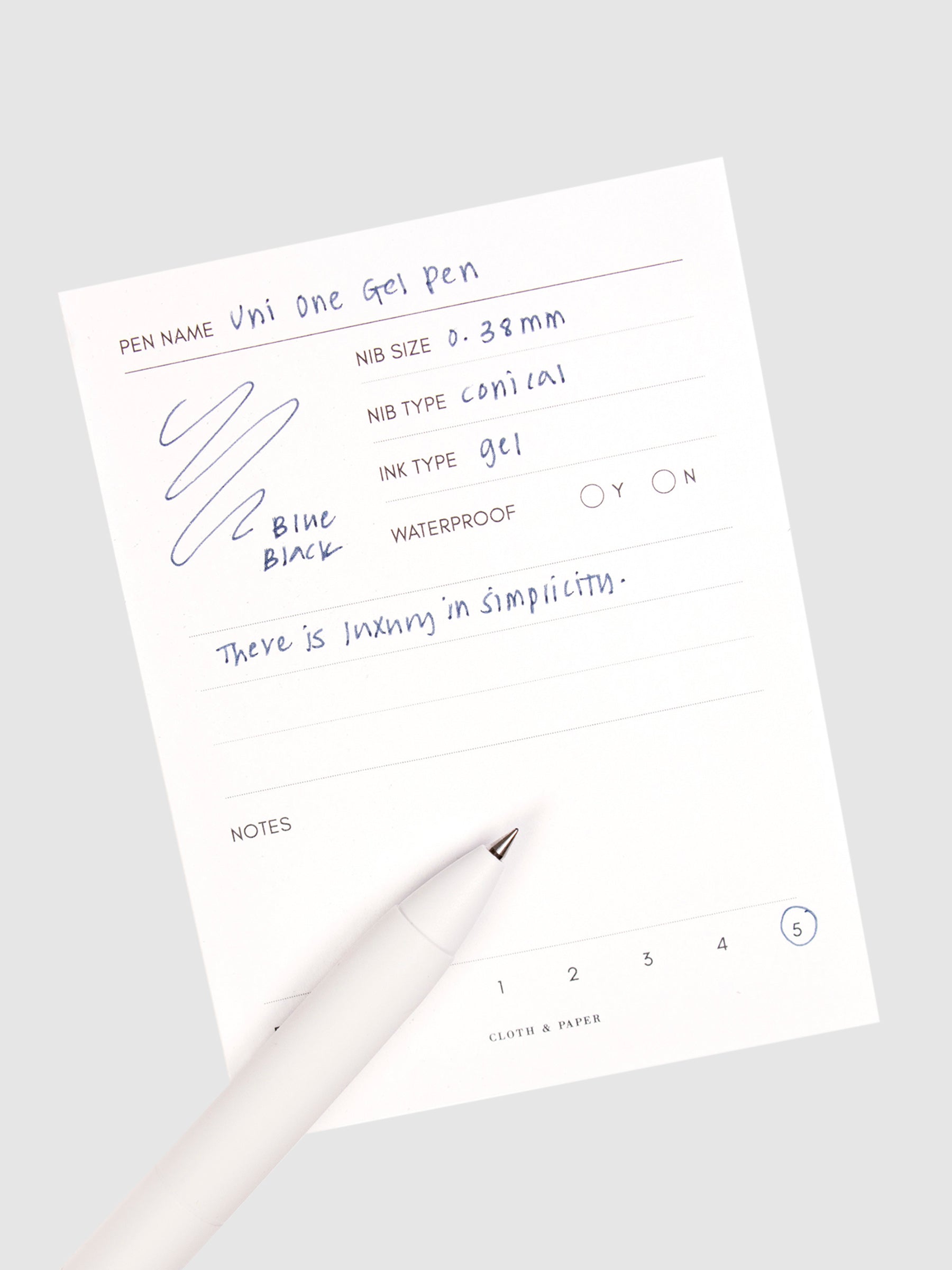 Blue Black pen resting on a pen test sheet displaying a writing sample detailing the pen's specs.