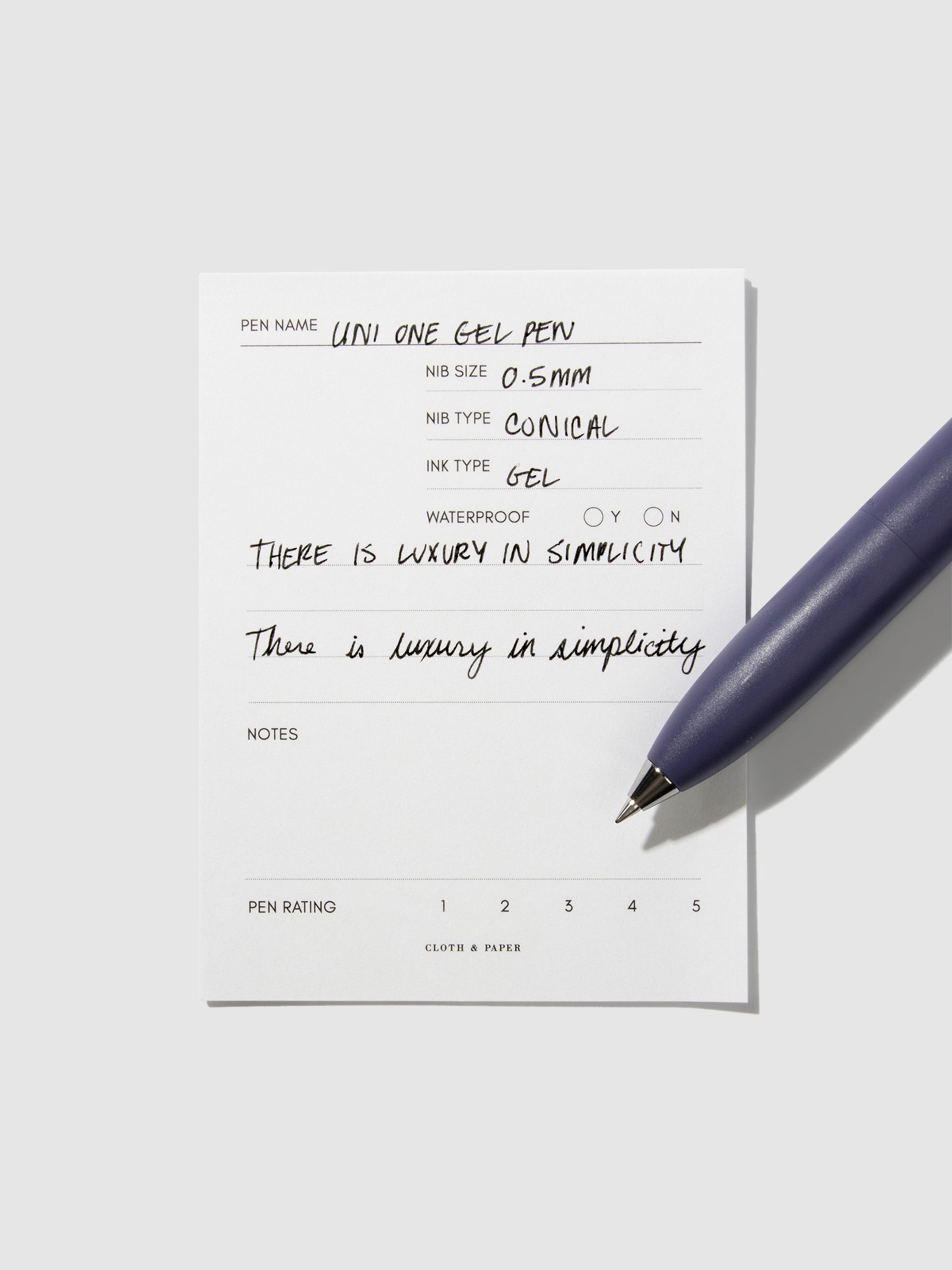 Uni-Ball One P pen resting on a pen test sheet. The sheet shows the pens specs. Color pictured is Grape.