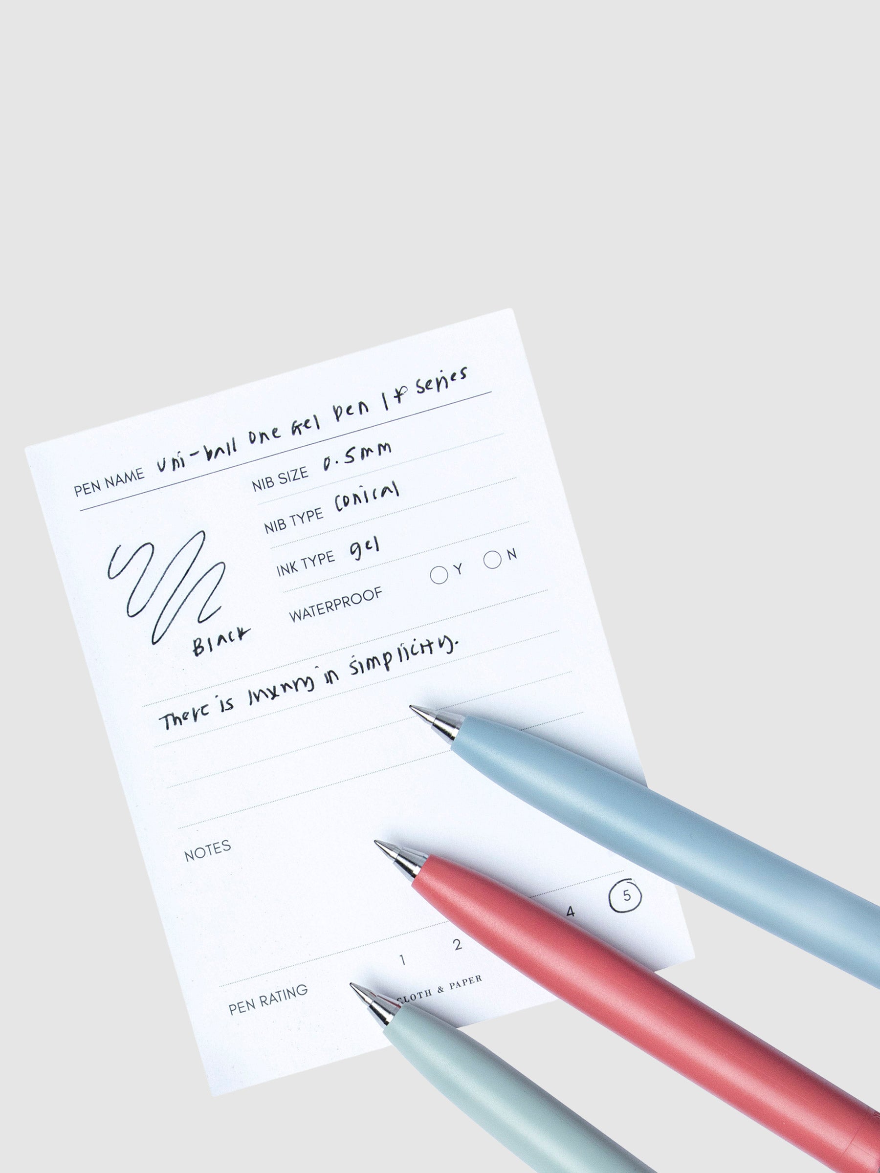 All three pen colors resting on a pen test sheet displaying a writing sample detailing the pen's specs.