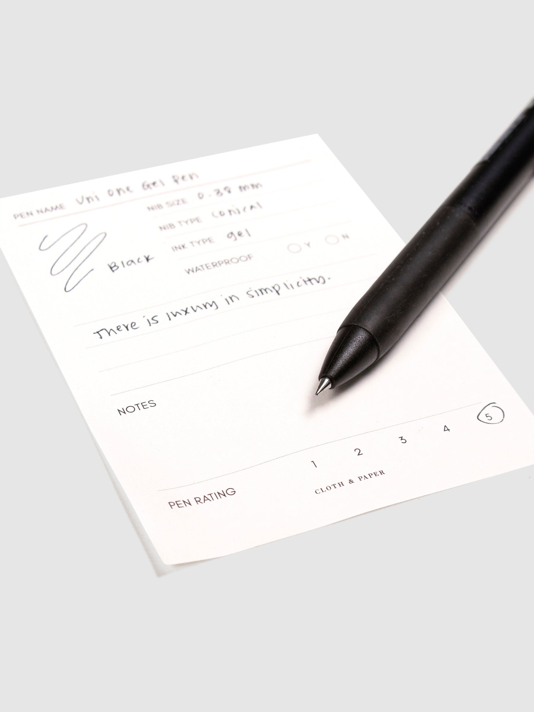 Uni One Gel Pen, 0.38 mm, Black Ink, Black Barrel, Cloth and Paper. Close up on pen nib resting on pen test sheet.