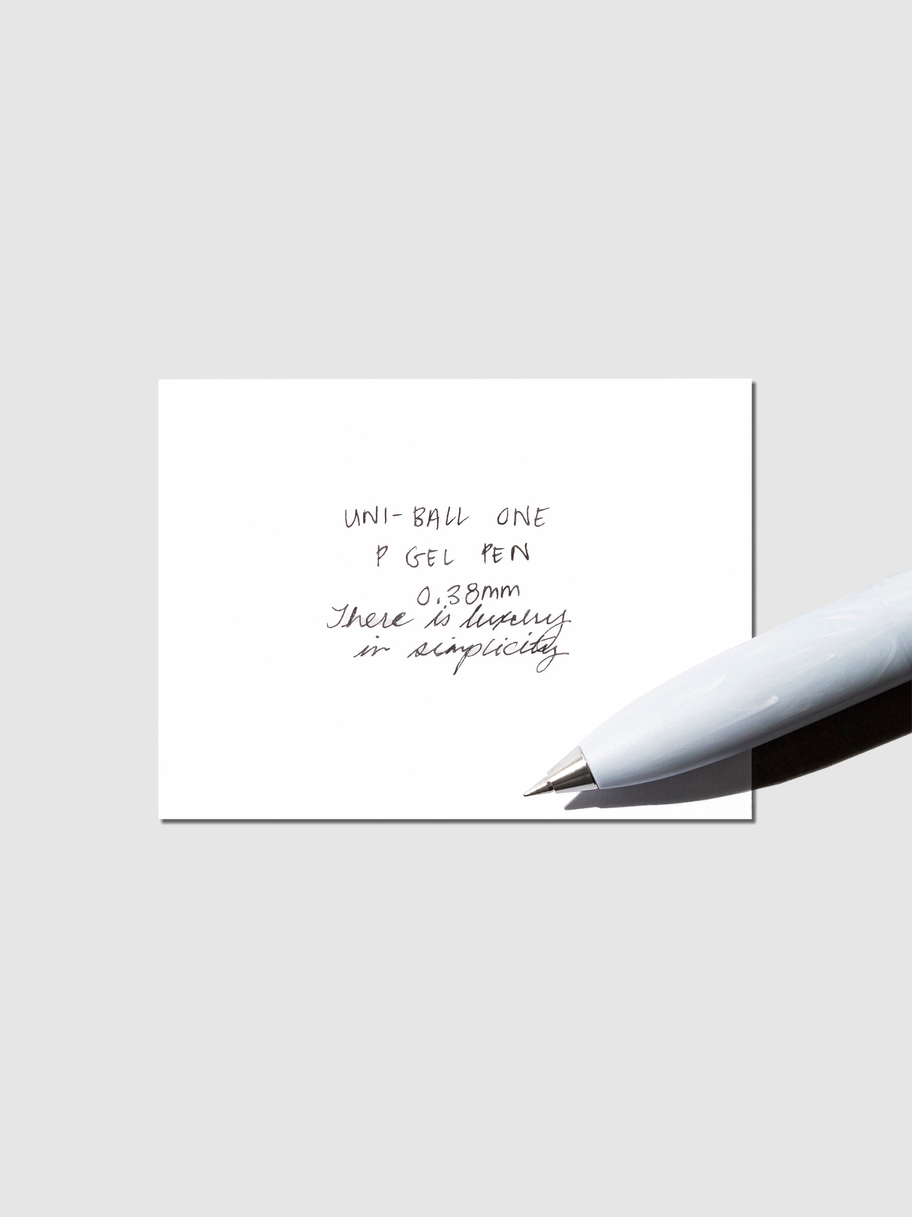 Uni-Ball One P pen resting on a pen test sheet. The sheet shows the pens specs. Color pictured is Savon.