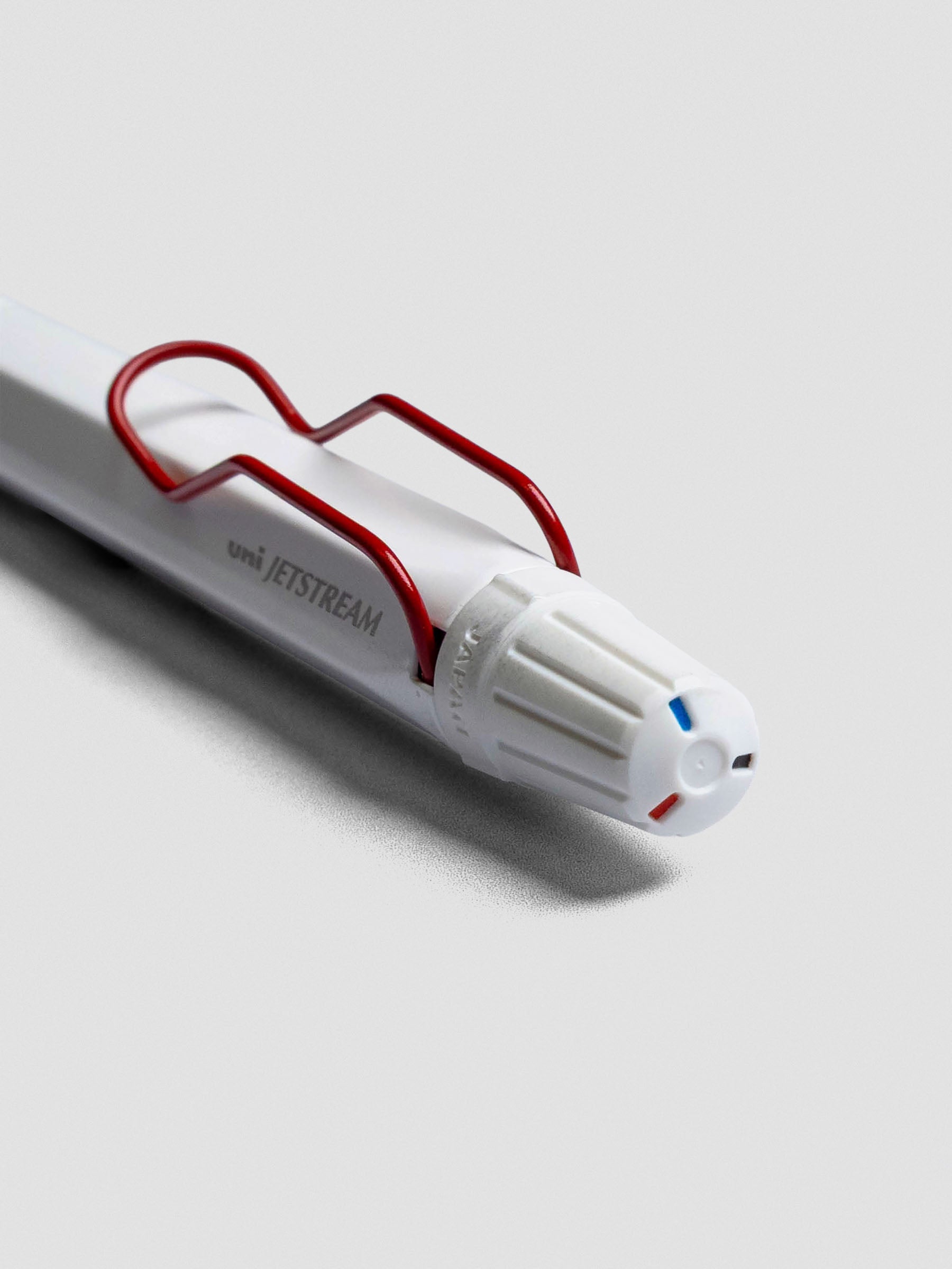 Close up of the top of a ballpoint mult-pen showing the white barrel, red clip, and dial selector to choose between red, blue, or black ink.