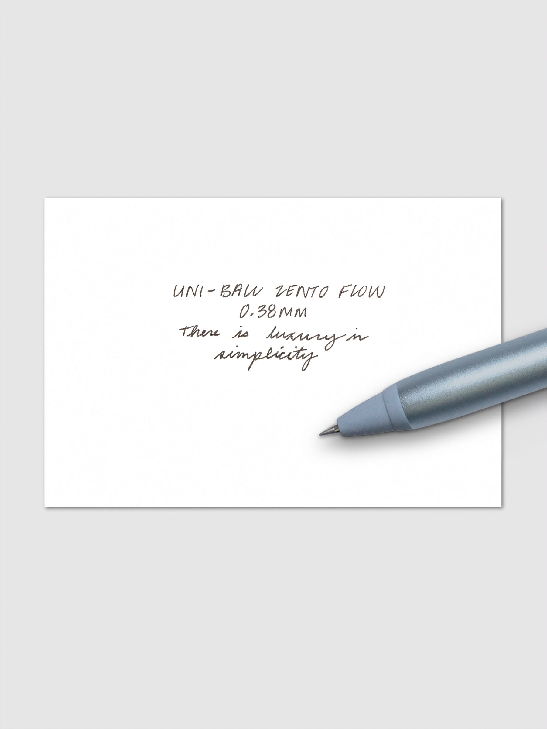 Handwritten writing sample using the Uni-ball Zento Flow Pen in a 0.38 mm nib. Shown with blue pen resting across paper.