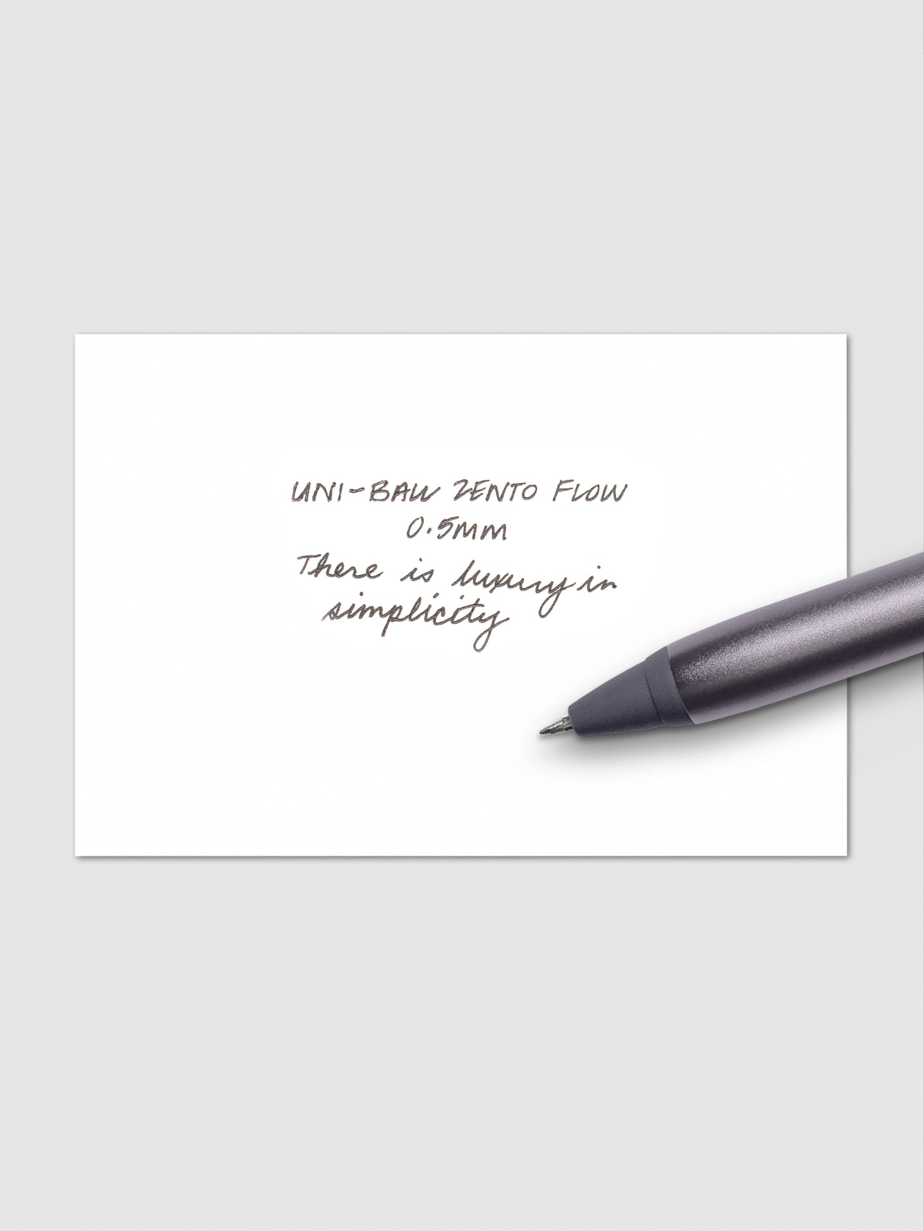 Handwritten writing sample using the Uni-ball Zento Flow Pen in a 0.5 mm nib. Shown with grey pen resting across paper.
