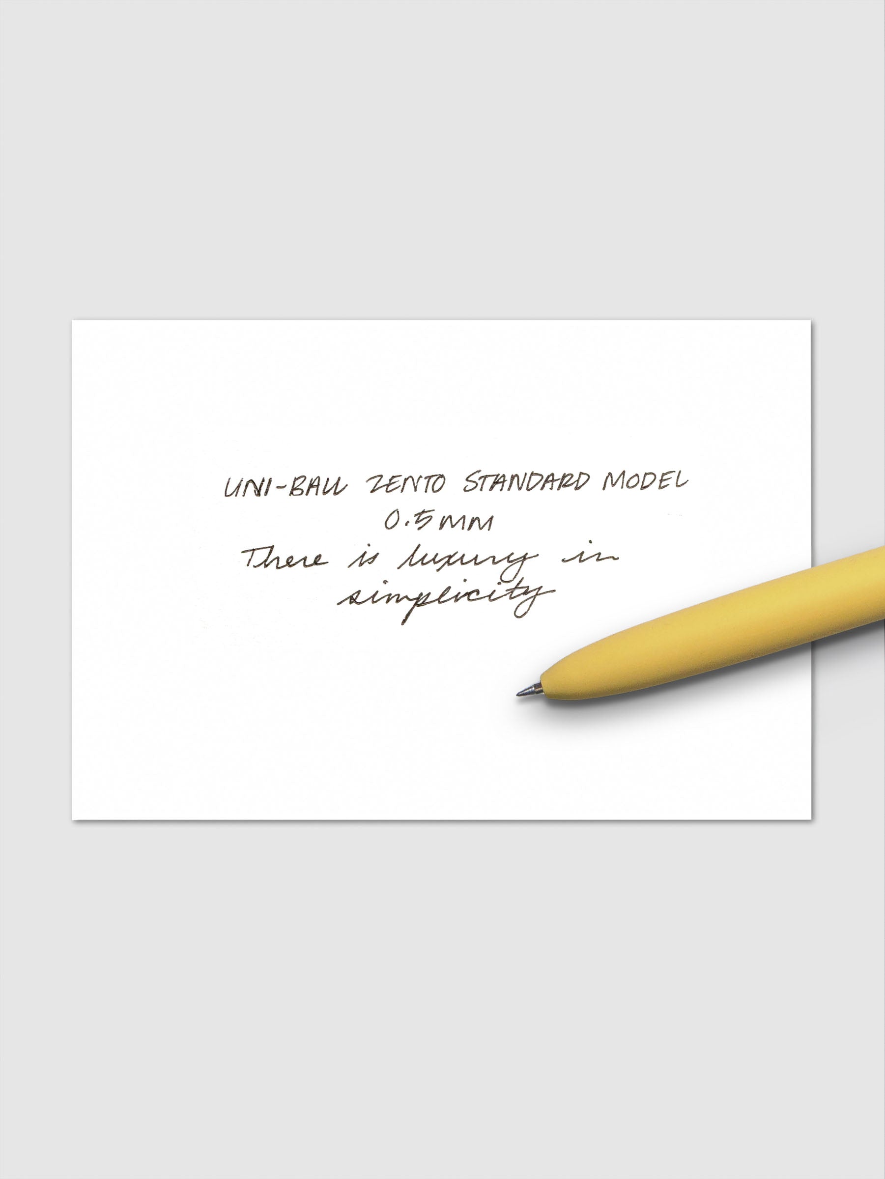 Handwritten sample using the Uni-ball Zento Standard Model Pen with black ink and a 0.5 mm nib. Shown with yellow pen resting across paper.