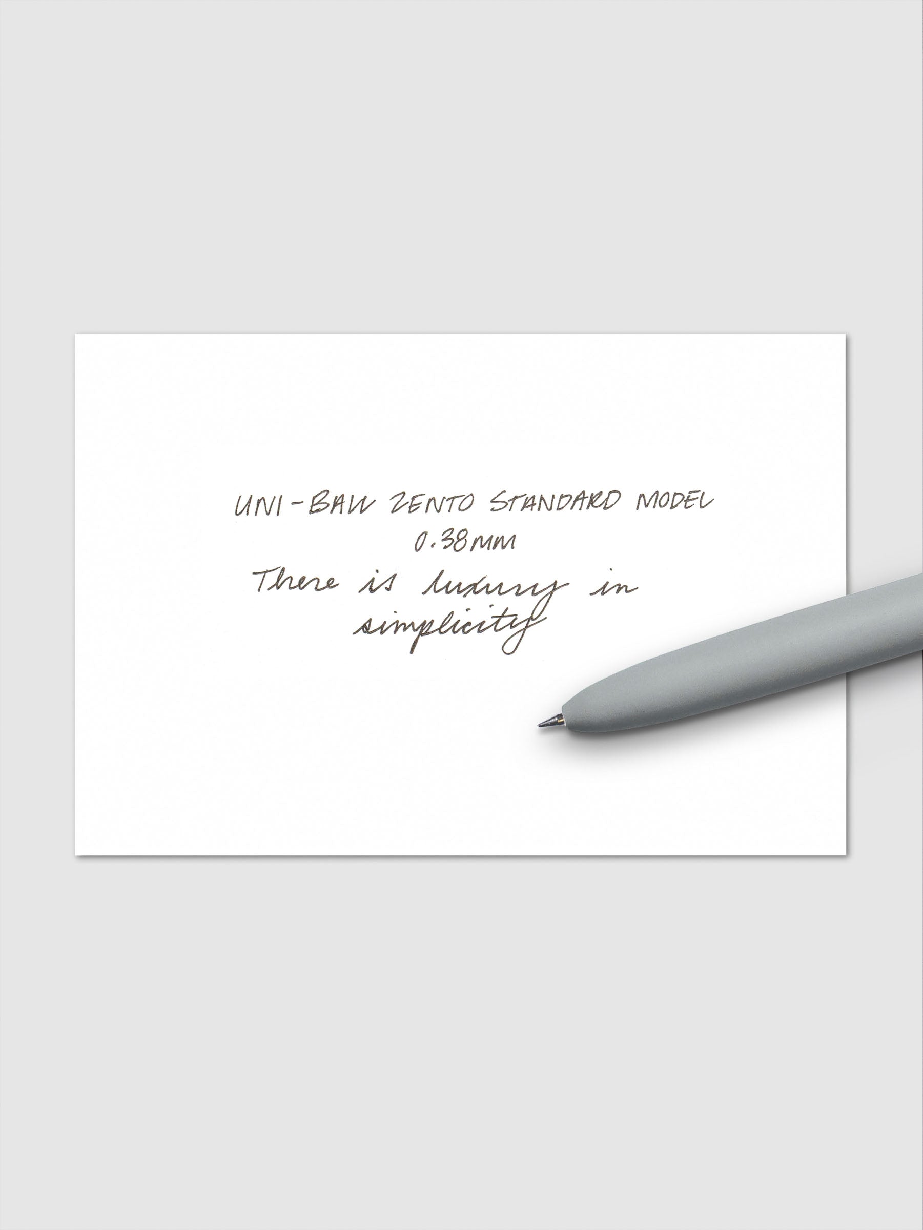 Handwritten sample using the Uni-ball Zento Standard Model Pen with black ink and a 0.38 mm nib. Shown with grey pen resting across paper.