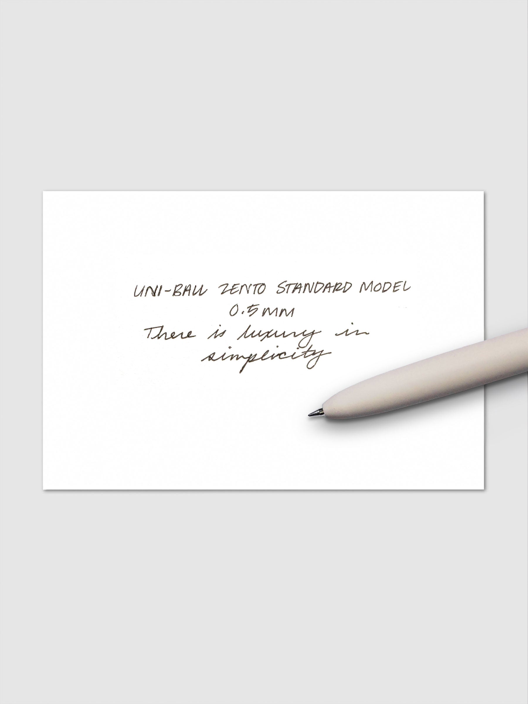 Handwritten sample using the Uni-ball Zento Standard Model Pen with black ink and a 0.5 mm nib. Shown with off-white pen resting across paper.
