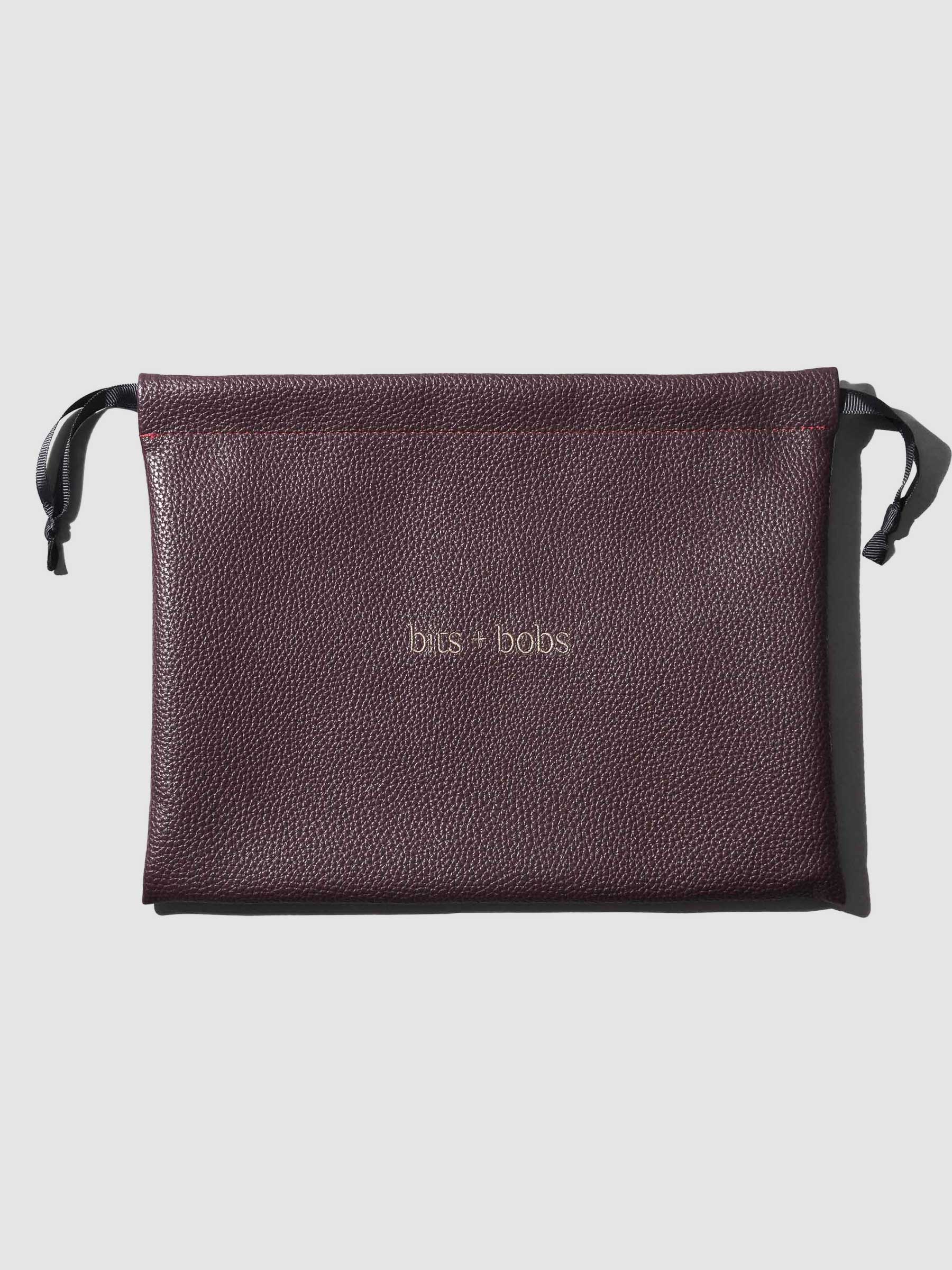 Front view of vegan leather dust bag in Bordeaux color with “bits + bobs” text, featuring side drawstring handles.