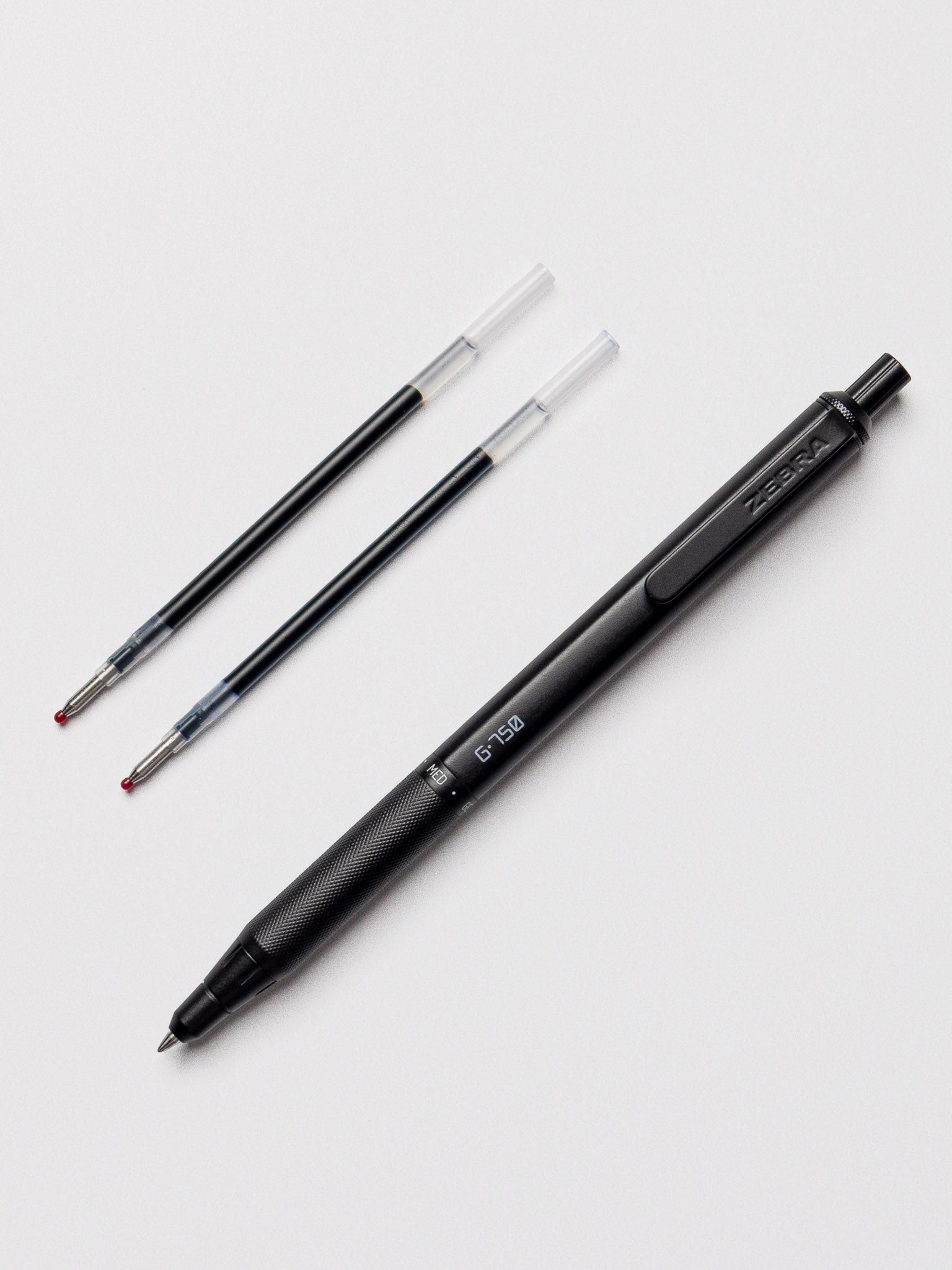 Zebra G-750 Retractable Gel Pen in black barrel displayed alongside two extra gel ink refills with protective caps, on a light gray background.