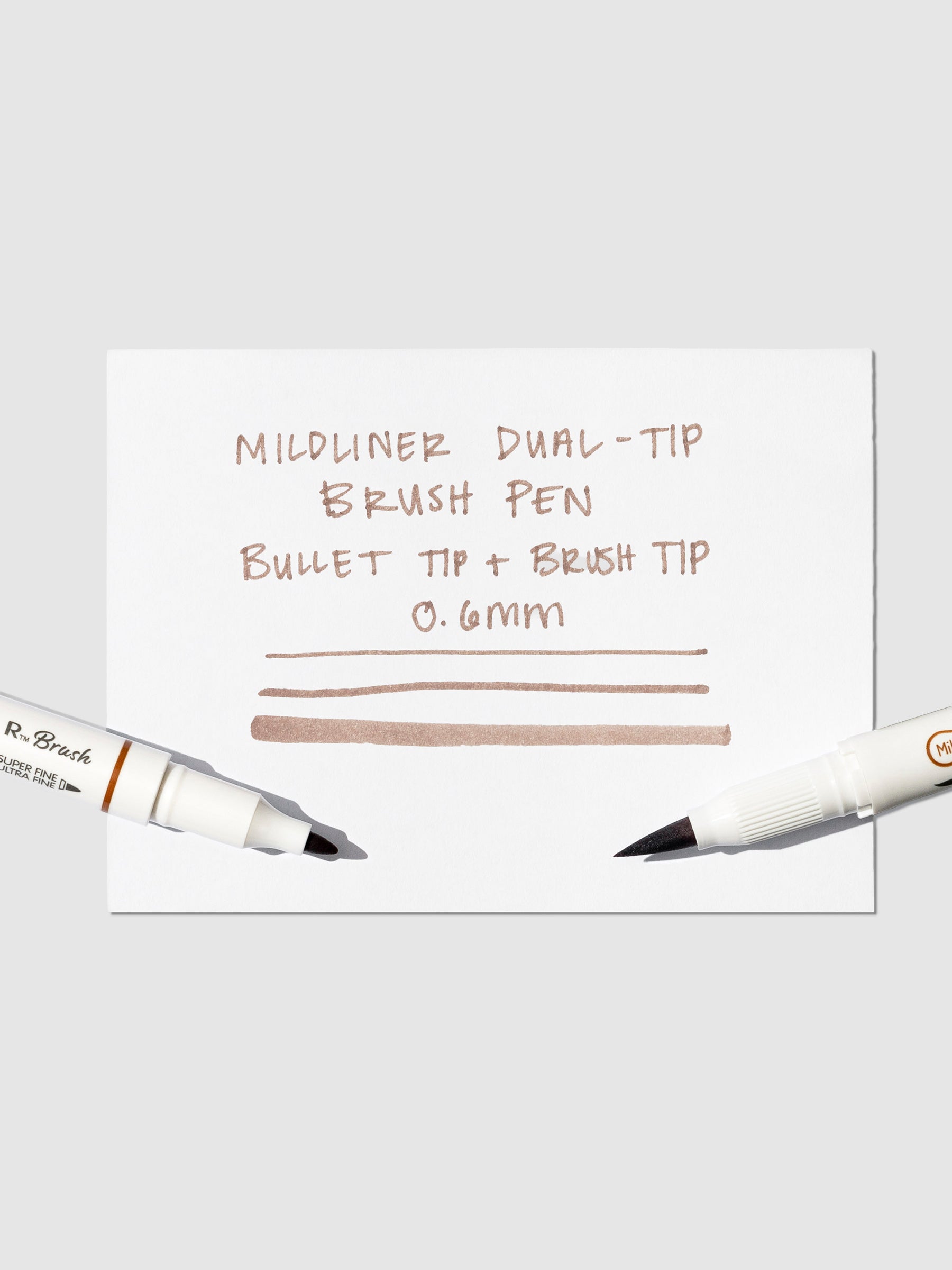 Brush pen tip resting on Brown pen test sheet displaying writing sample that details pen specs.