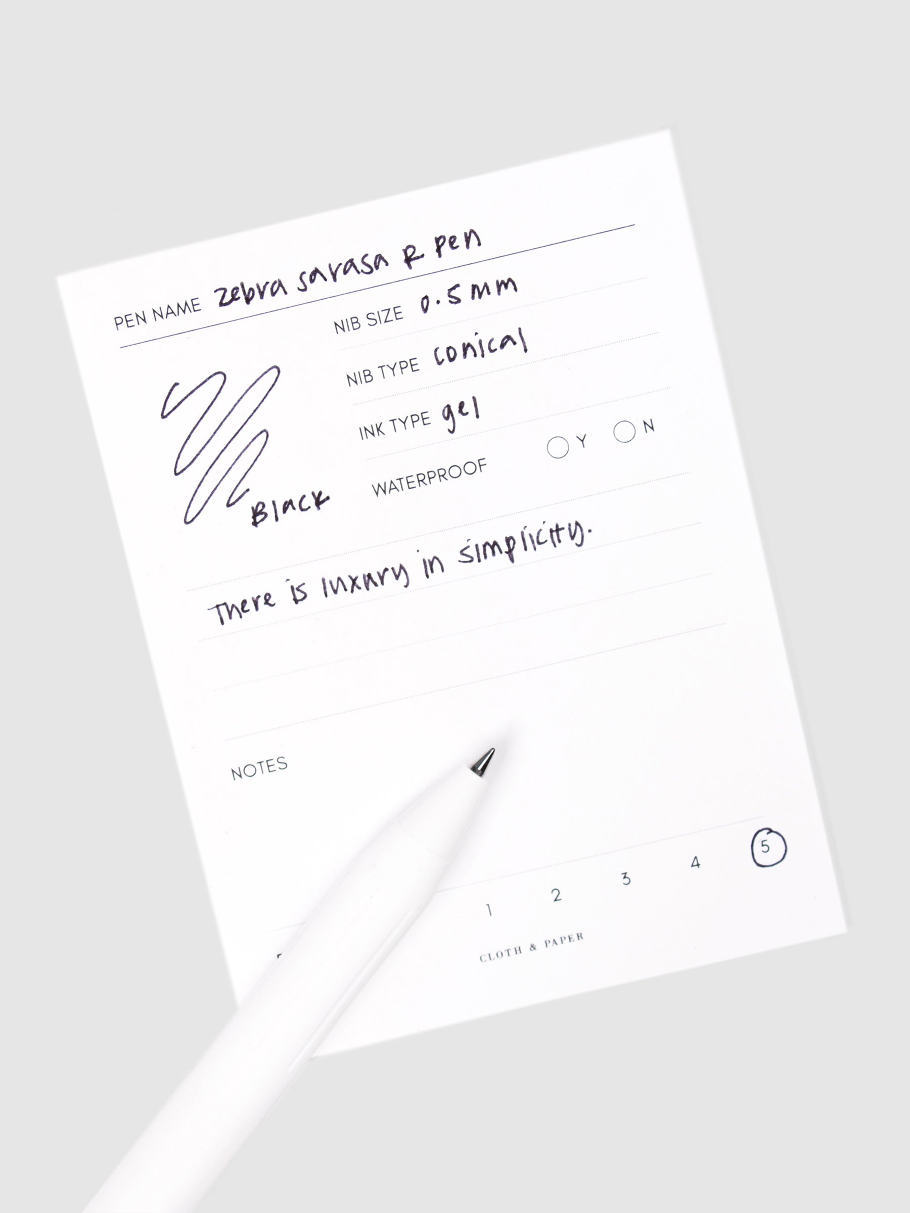 Zebra Sarasa R Pen, 0.5 mm, Black, Cloth and Paper. Pen resting on pen test sheet displaying writing sample.