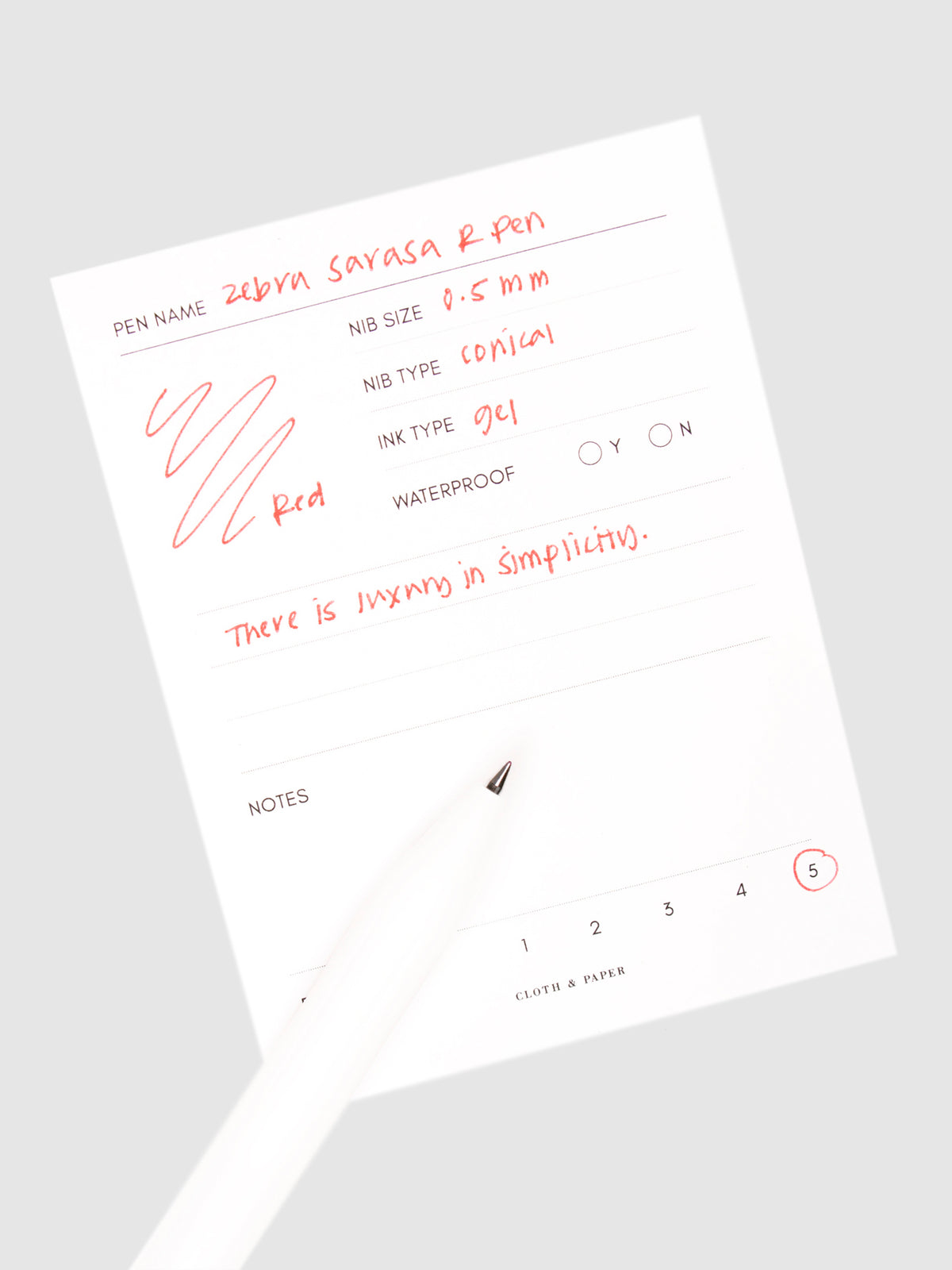 Zebra Sarasa R Pen, 0.5 mm, Red, Cloth and Paper. Pen resting on pen test sheet displaying writing sample.