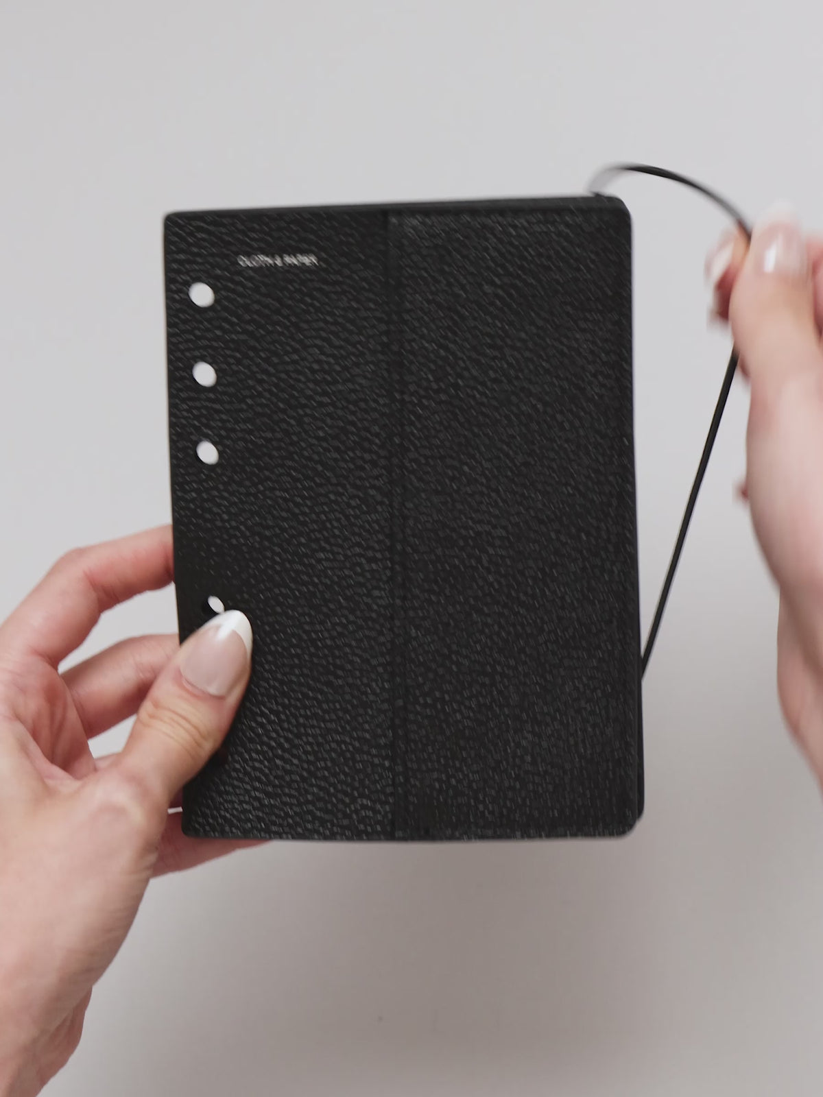 Video of the A5 6-Ring Punch Genuine Leather Planner Cover Set, showing pebbled black leather, the silver foiled logo at the top left, the punch holes down the left edge, and the bungee cord running down the right