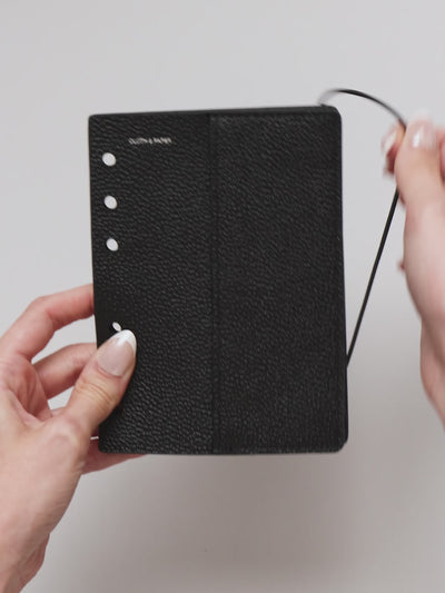 Video of the A5 6-Ring Punch Genuine Leather Planner Cover Set, showing pebbled black leather, the silver foiled logo at the top left, the punch holes down the left edge, and the bungee cord running down the right