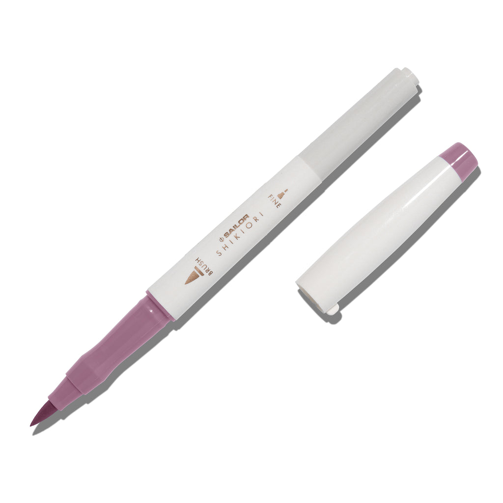 Brush pen displayed on a white background. It is uncapped with its brush nib exposed, and the cap lying parallel to the marker. Color pictured is Yozakura. 