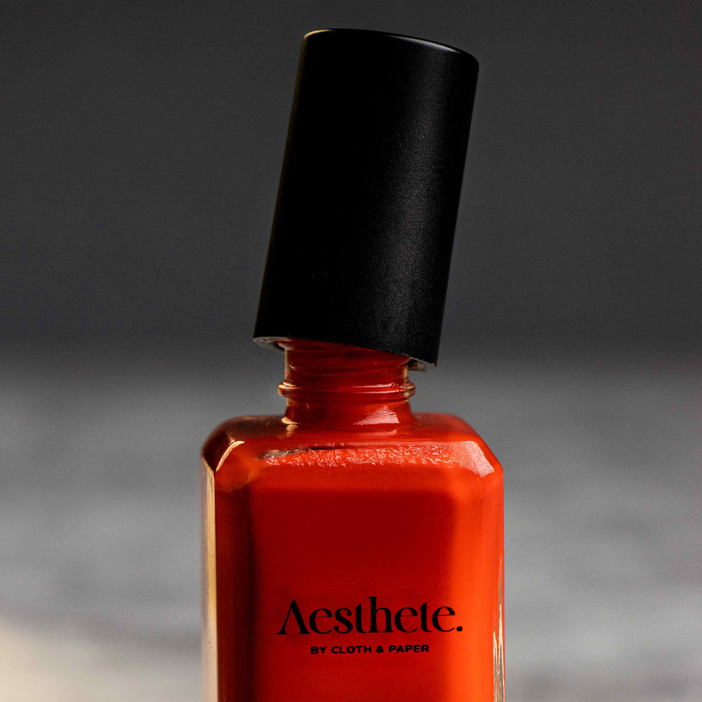 Red nail polish bottle with its cap slightly untwisted.