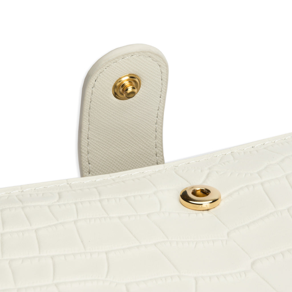 Close up on the snap detail of a white croc leather agenda cover with gold snap hardware.