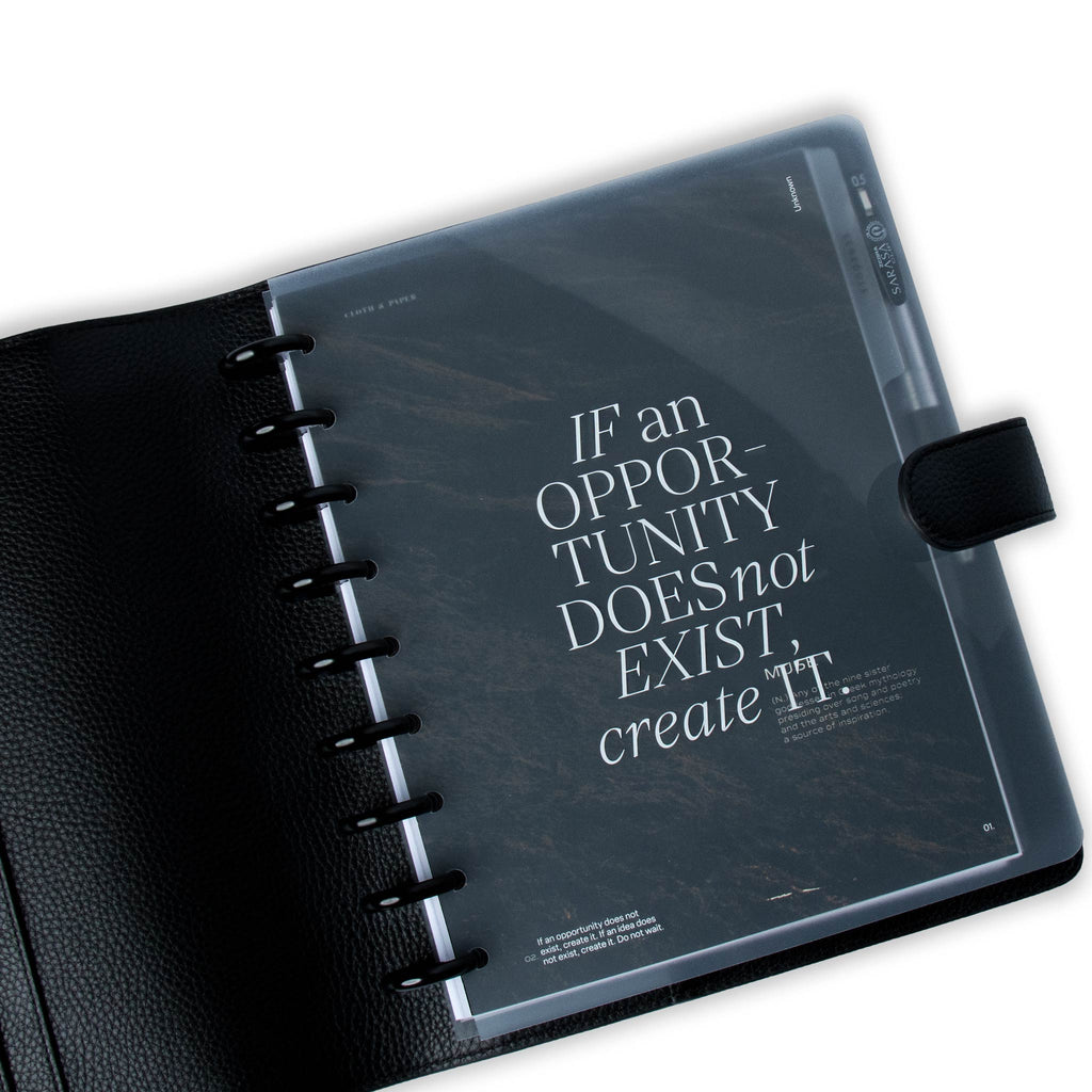 Glass Plastic Discbound Notebook Cover in Opportunity design styled inside a black leather agenda cover. The cover is used on a discbound system with black discs, layered over top of the Muse Dashboard.
