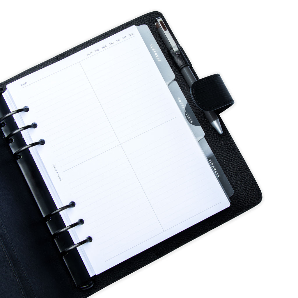 Quad Lined Planner Inserts styled inside a black leather agenda with Essentials Dividers underneath. The agenda has a gray pen in its pen loop.