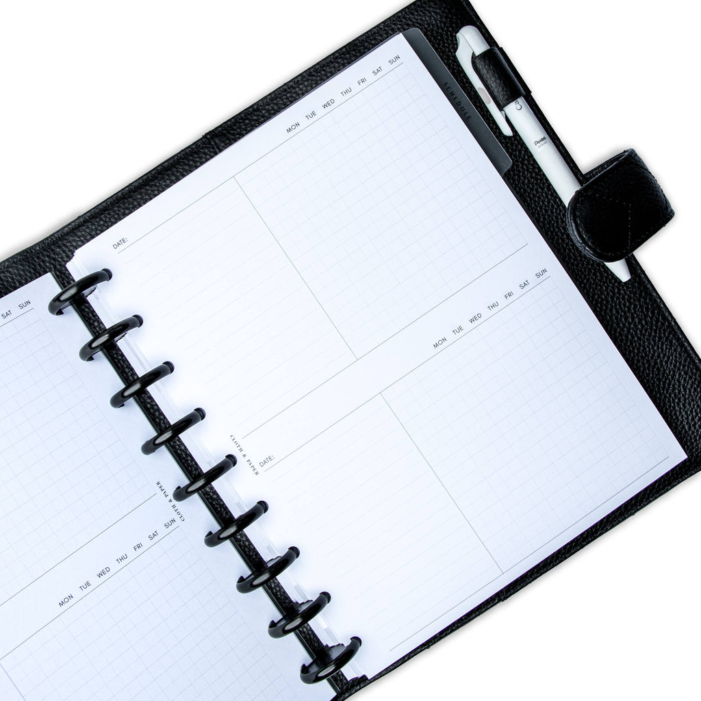 Undated Task Duo Note Planner Inserts styled inside a discbound planner in a black leather agenda cover. The discbound planner has black discs, and there is a white pen tucked into the agenda cover's pen loop.